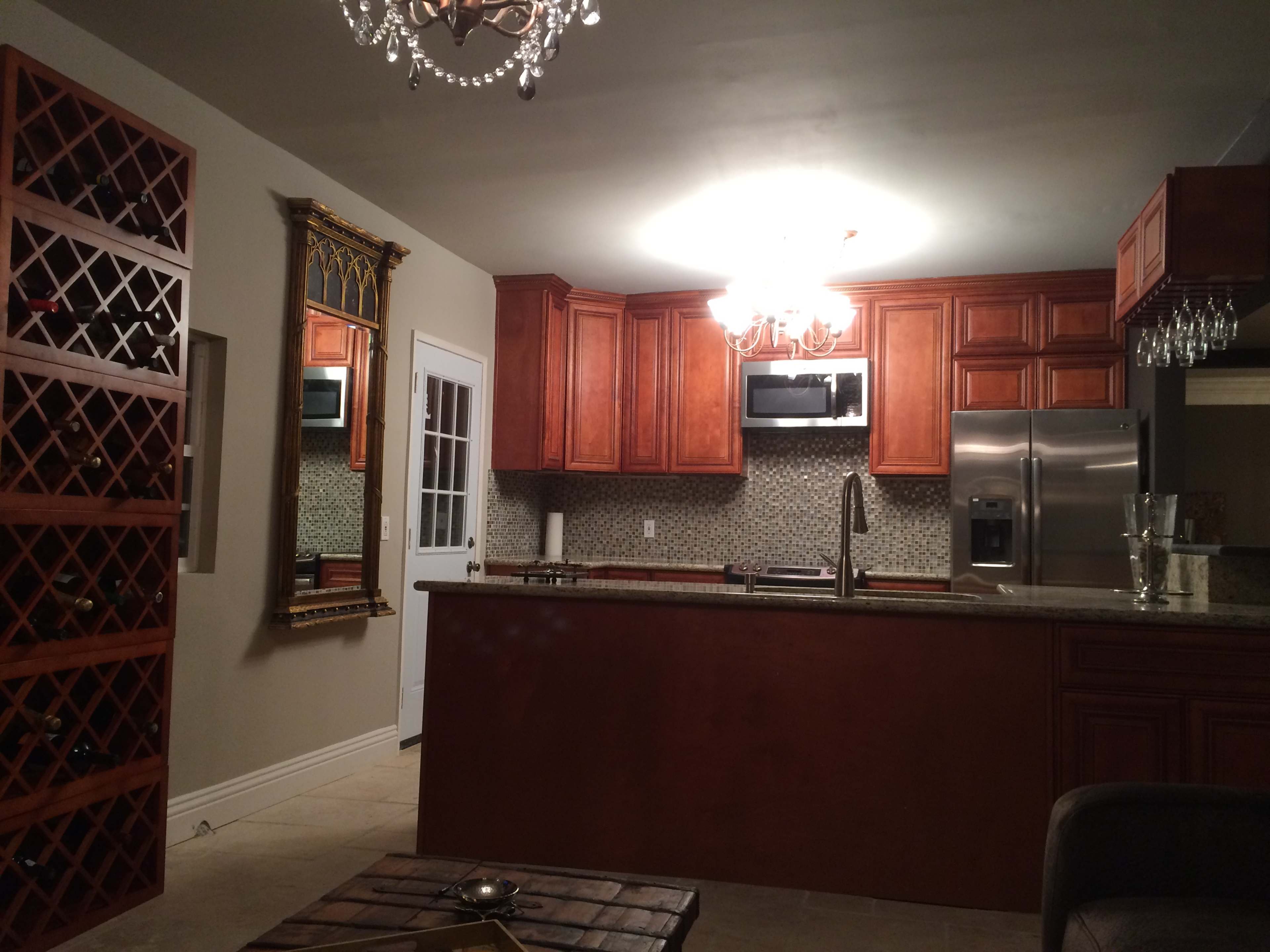 A kitchen with wooden cabinetry, a wine rack, stainless steel appliances, and a chandelier.
