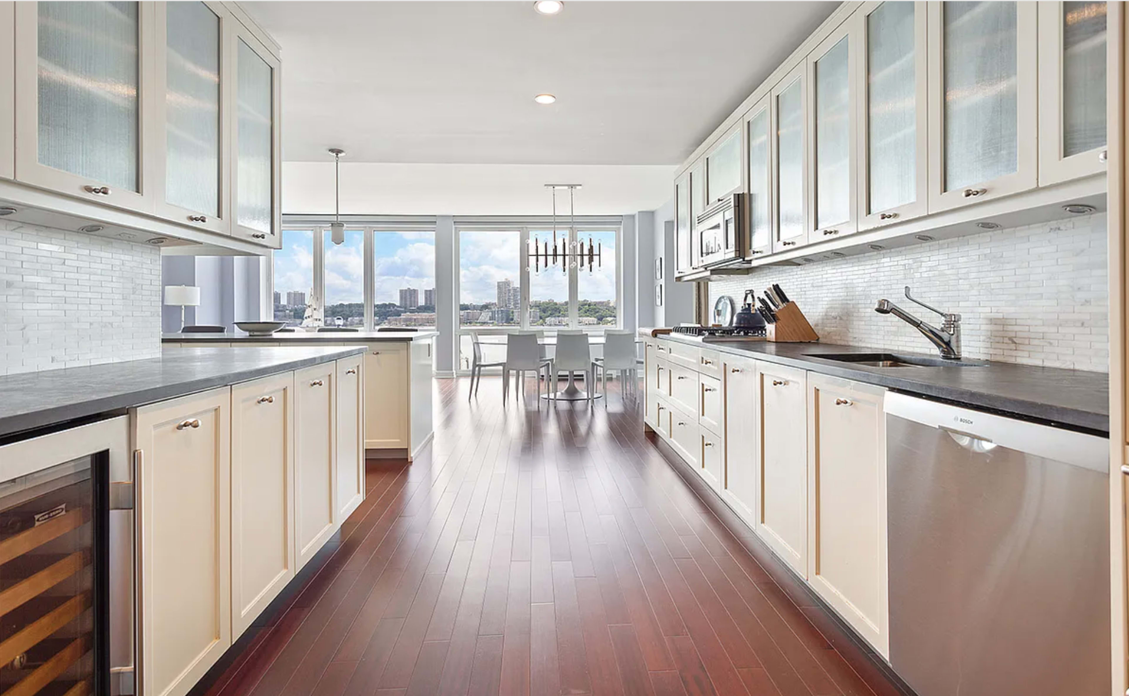 A modern kitchen with white cabinetry, dark countertops, and a view of a dining area through a large window.
