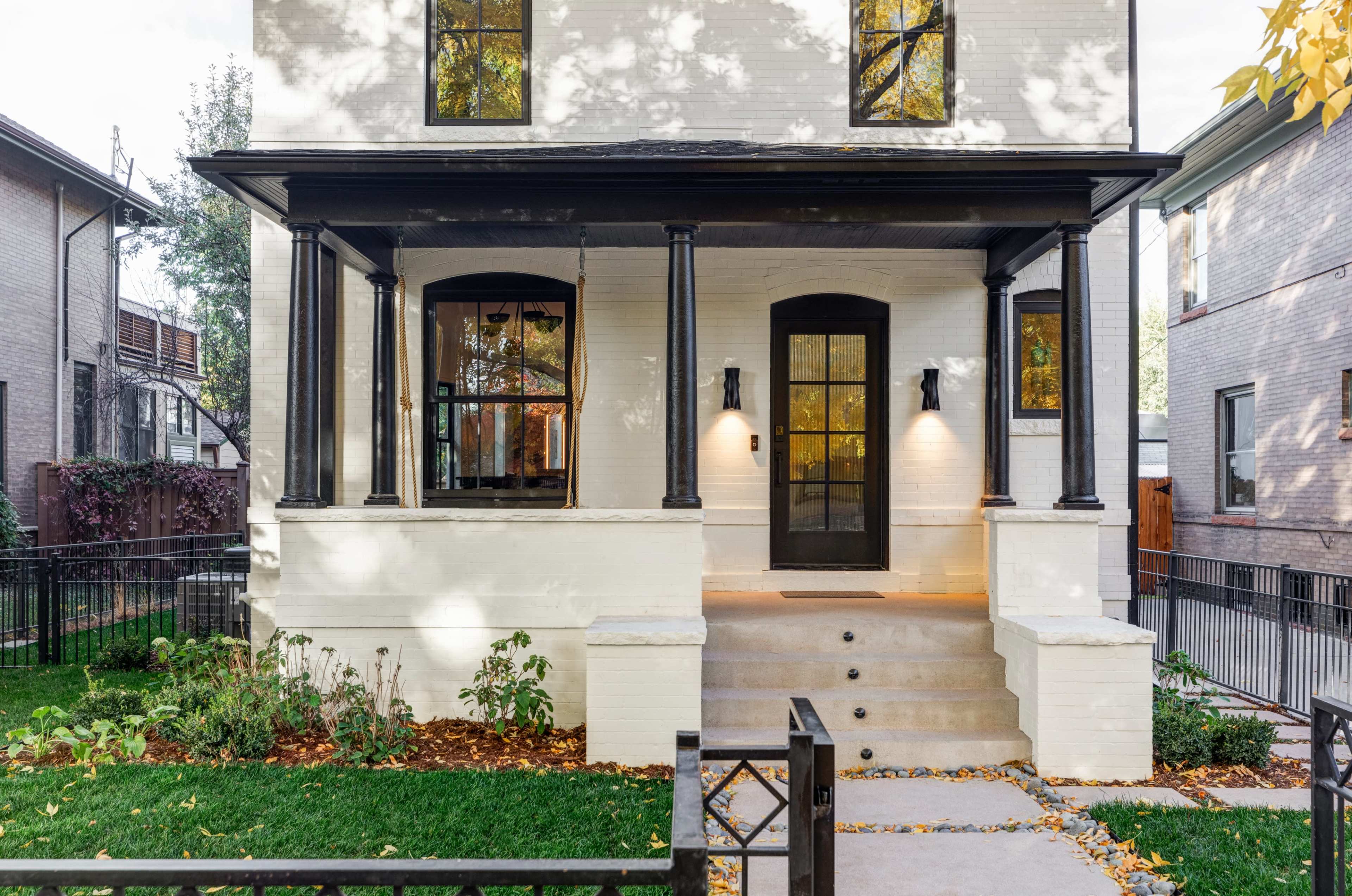 The image shows a modern two-story house with a black porch and large front steps, framed by a neatly landscaped yard.