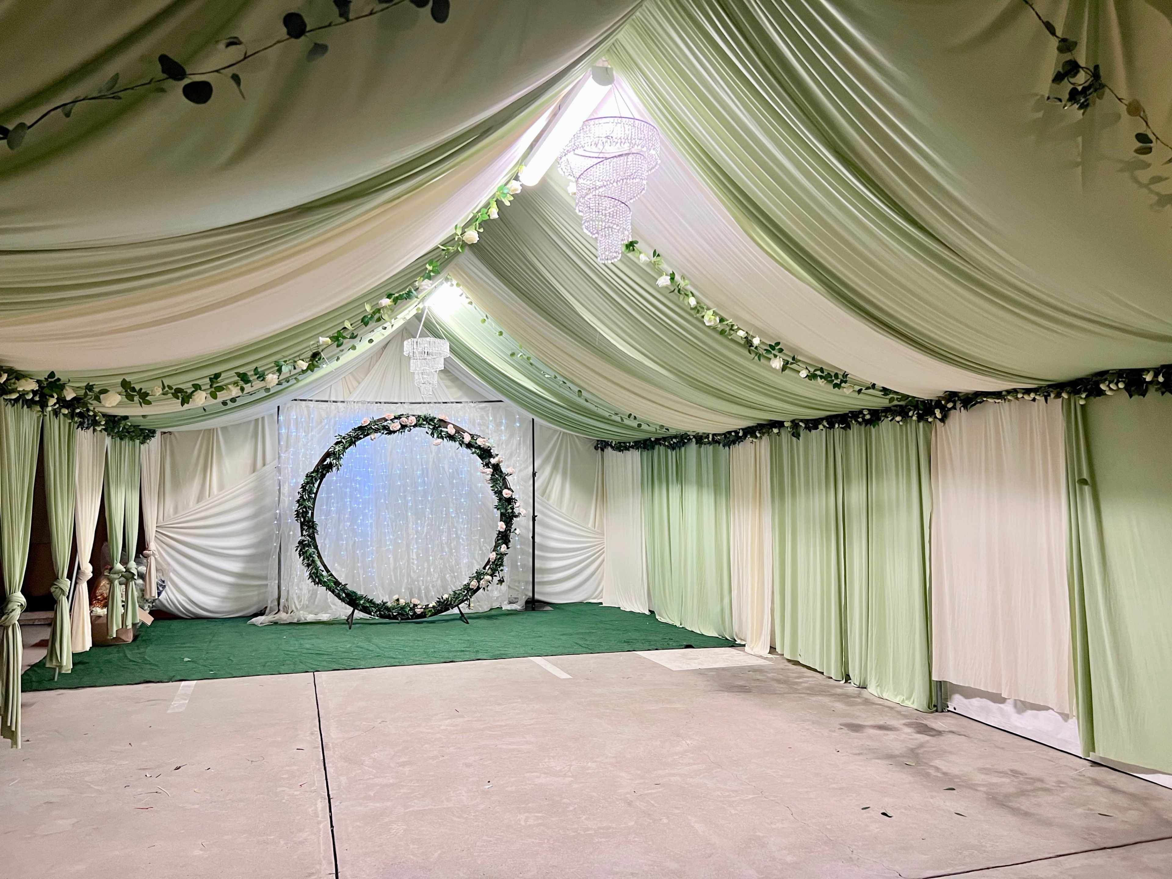 An indoor venue decorated with green and white drapes, featuring a floral circular backdrop at the far end.