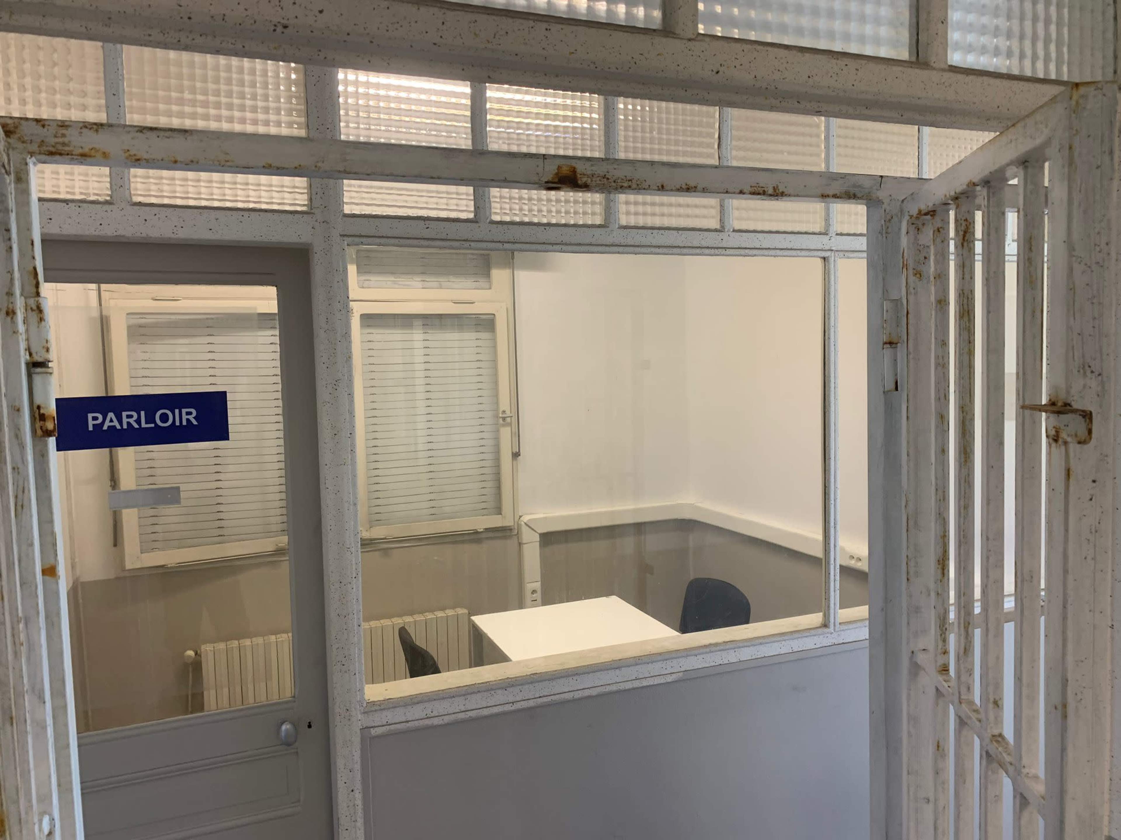 A view through a metal gate into a small, empty room with a table and a chair, labeled "PARLOIR."