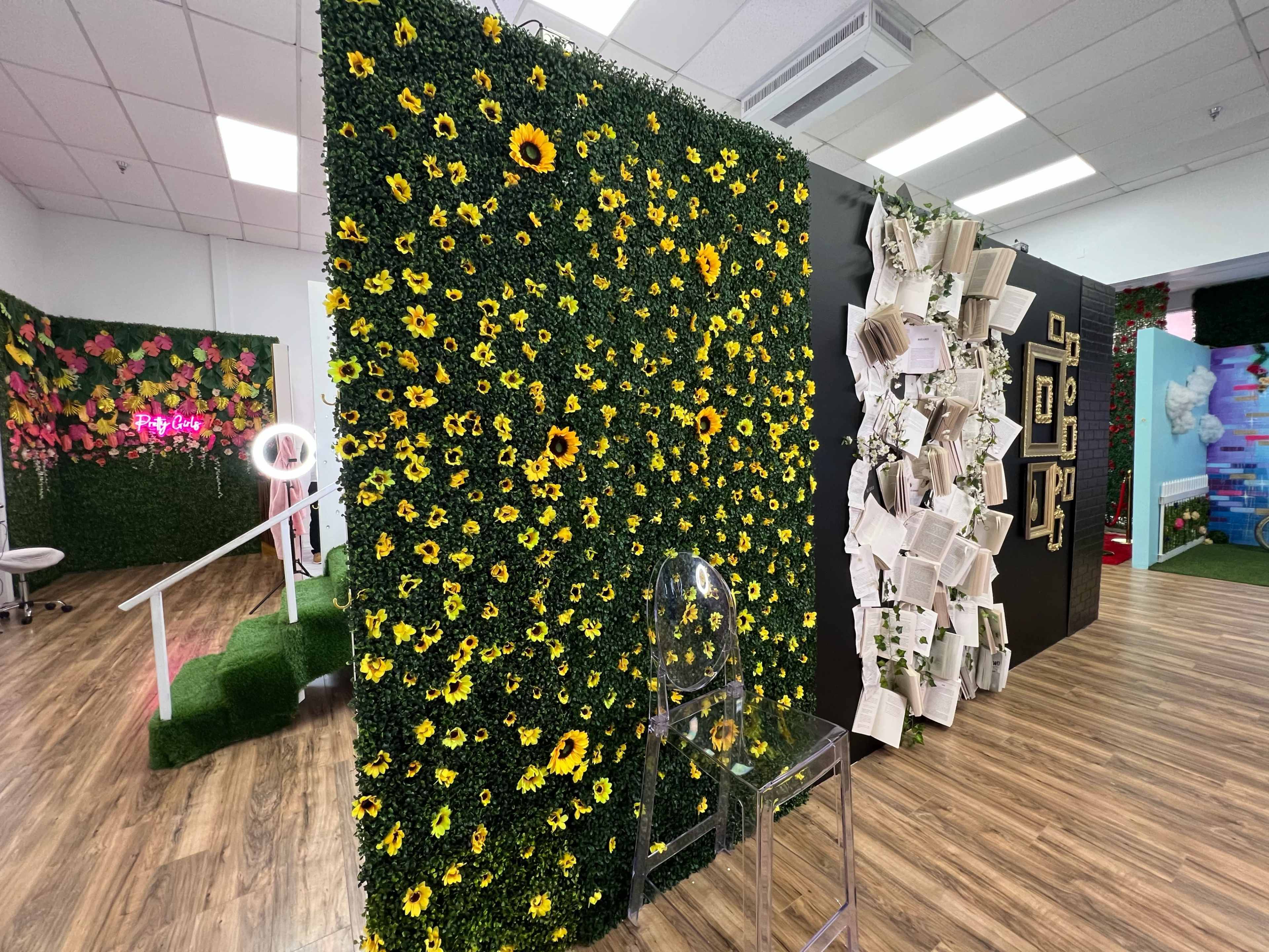 A decorative room with a floral wall of artificial sunflowers and an adjacent wall adorned with framed pictures and hanging pages.