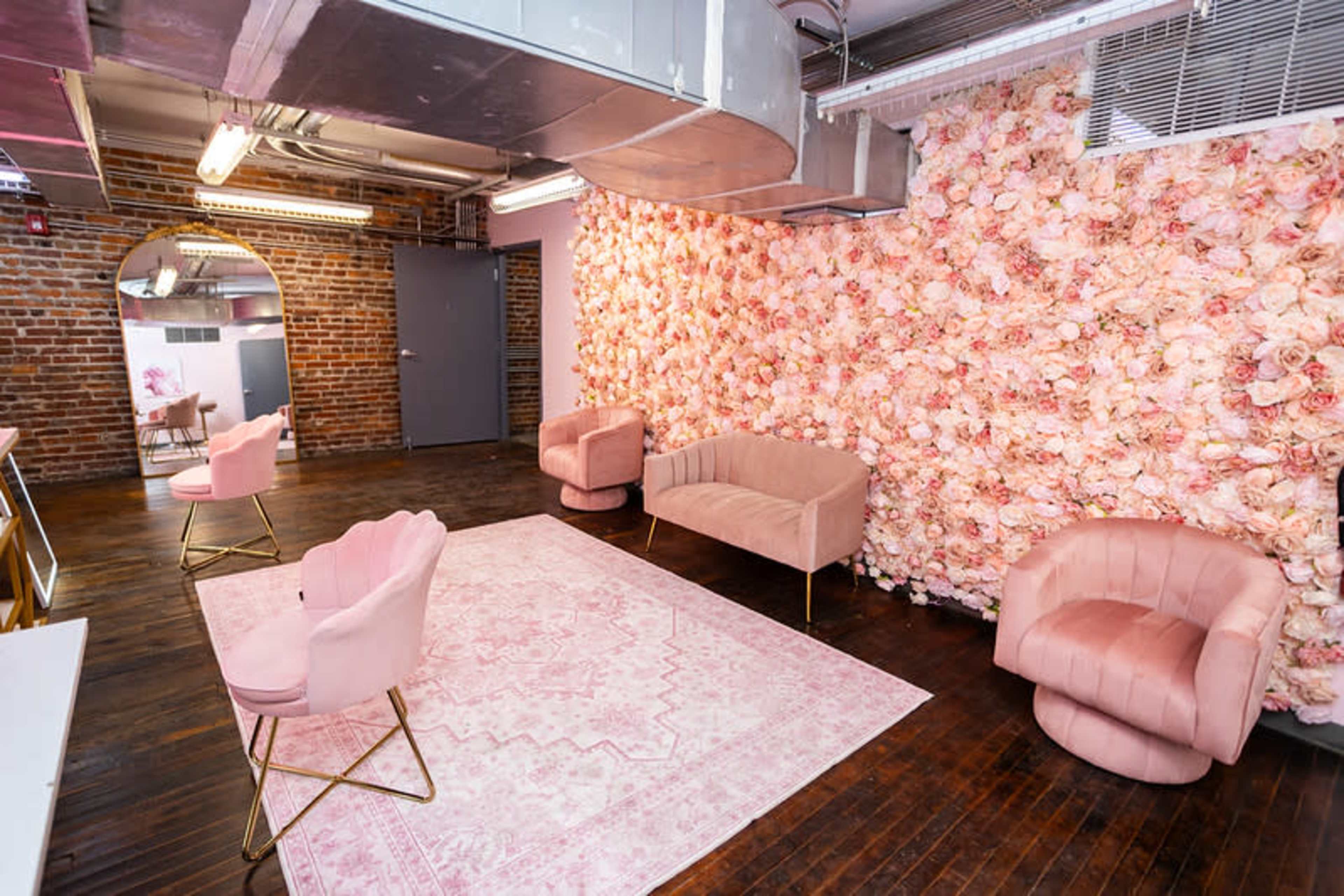 The interior features a cozy lounge with pink upholstered chairs, a floral wall, and a patterned area rug on wooden flooring.