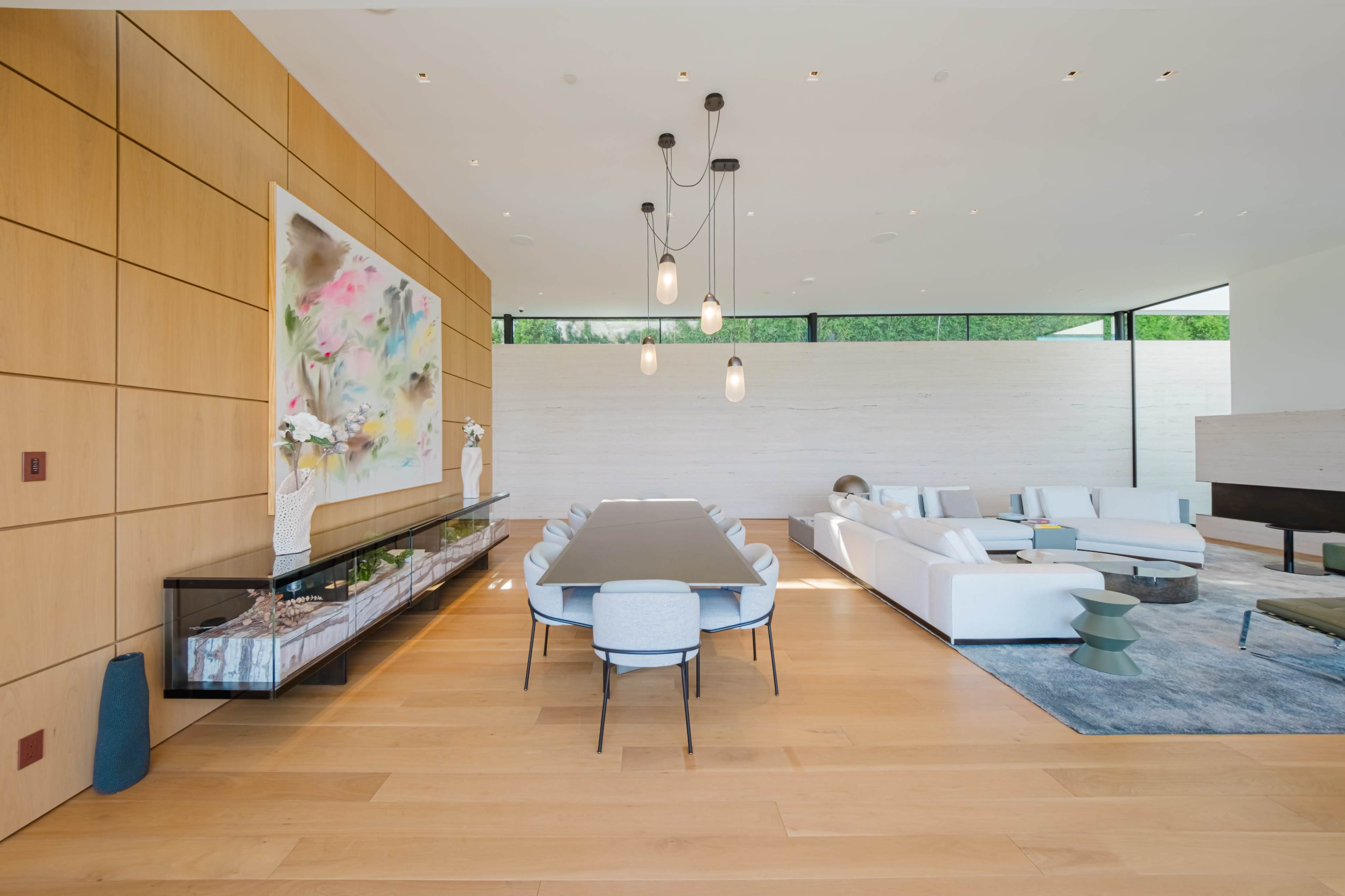A modern living space featuring a dining area with a long table and chairs, adjacent to a seating area with a large sofa, illuminated by pendant lights.