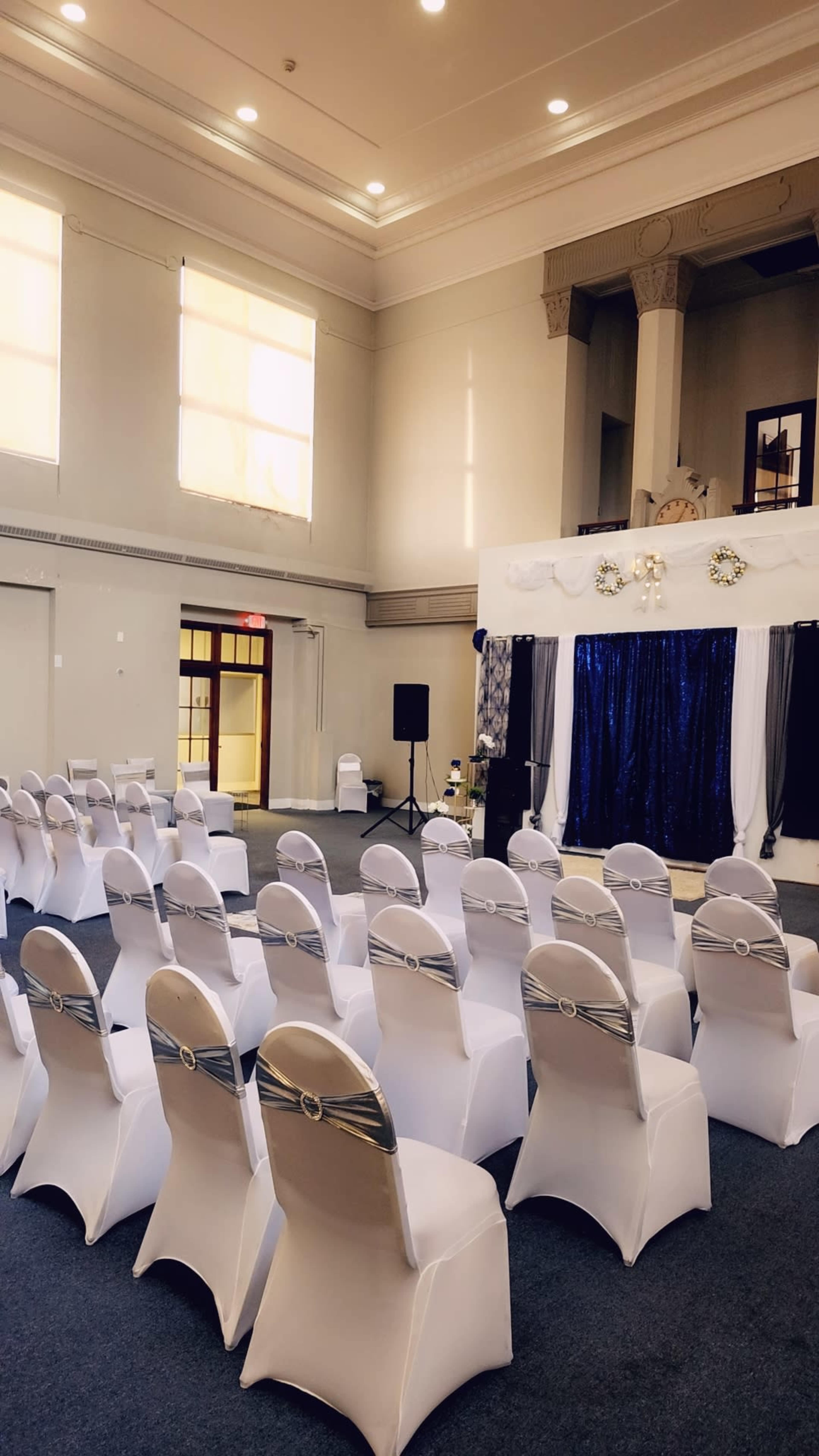 An indoor venue arranged with white chairs facing a decorated stage draped in blue fabric.