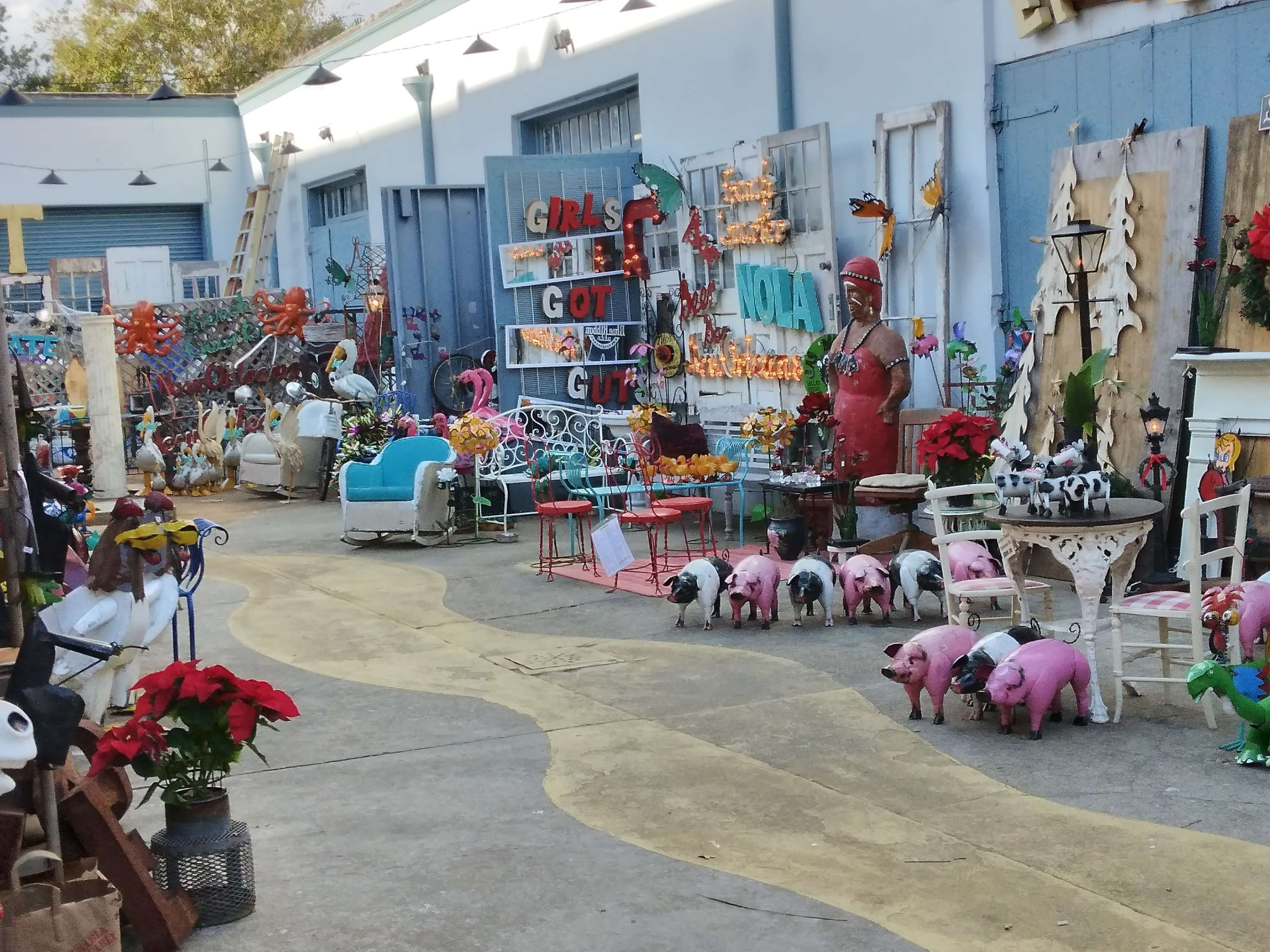 The image shows a vibrant outdoor marketplace filled with various colorful decorations, eclectic garden ornaments, and furniture arranged along a winding pathway.