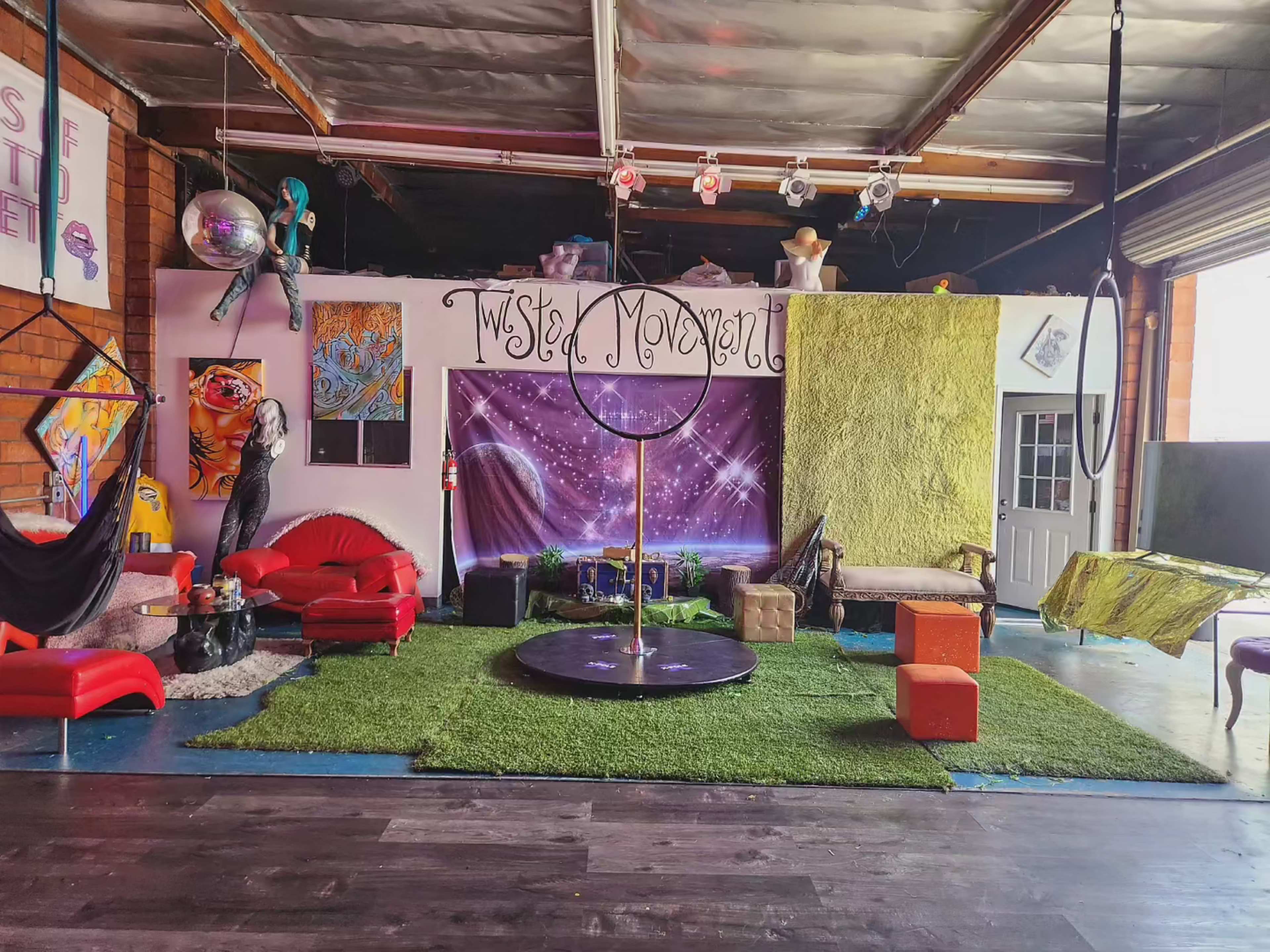 The image shows a vibrant studio space decorated with colorful furniture, a circular stage in the center, and various artistic elements on the walls.