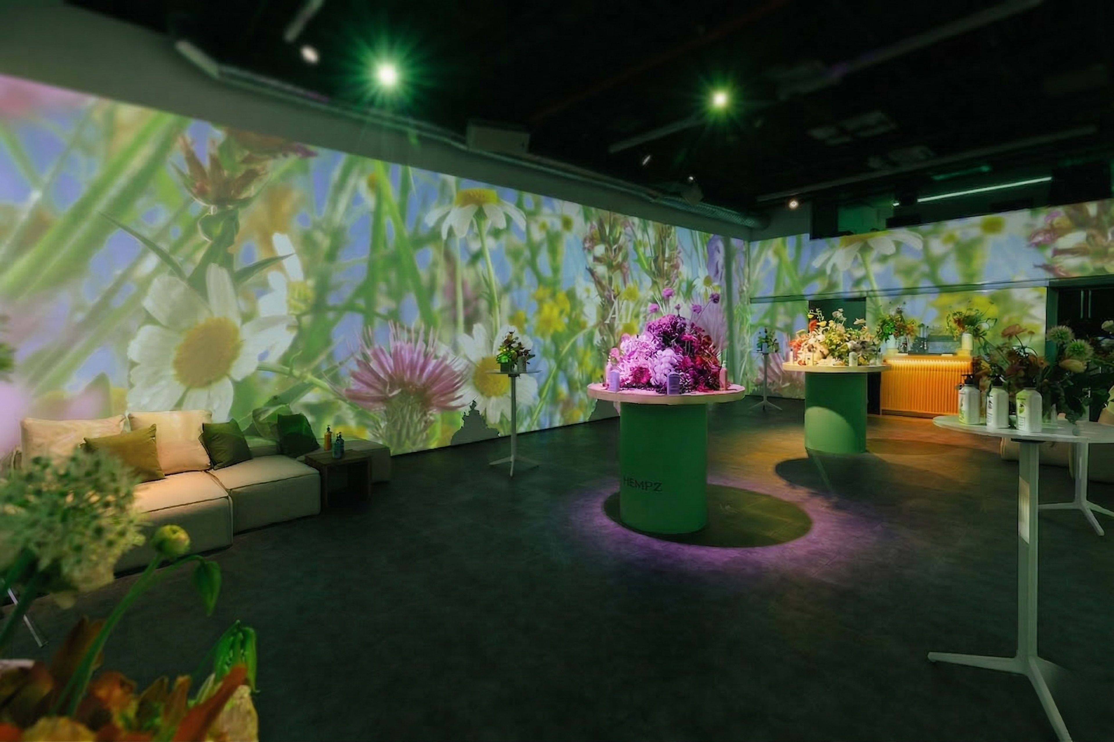 The image shows a modern floral display area with projected images of flowers on the walls and various flower arrangements on circular tables.