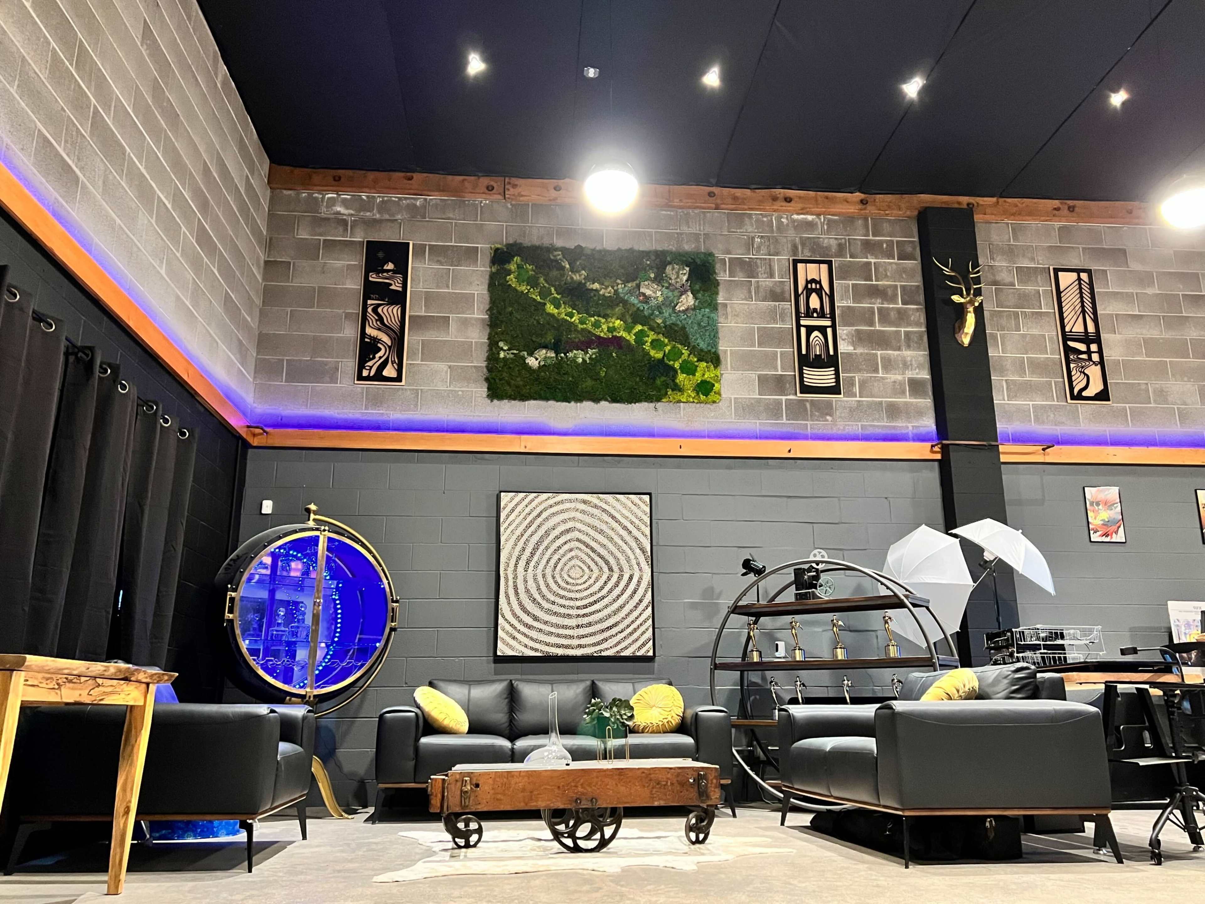 The interior of a modern lounge space features black leather sofas, a circular coffee table, decorative wall art, and a mix of ambient lighting.