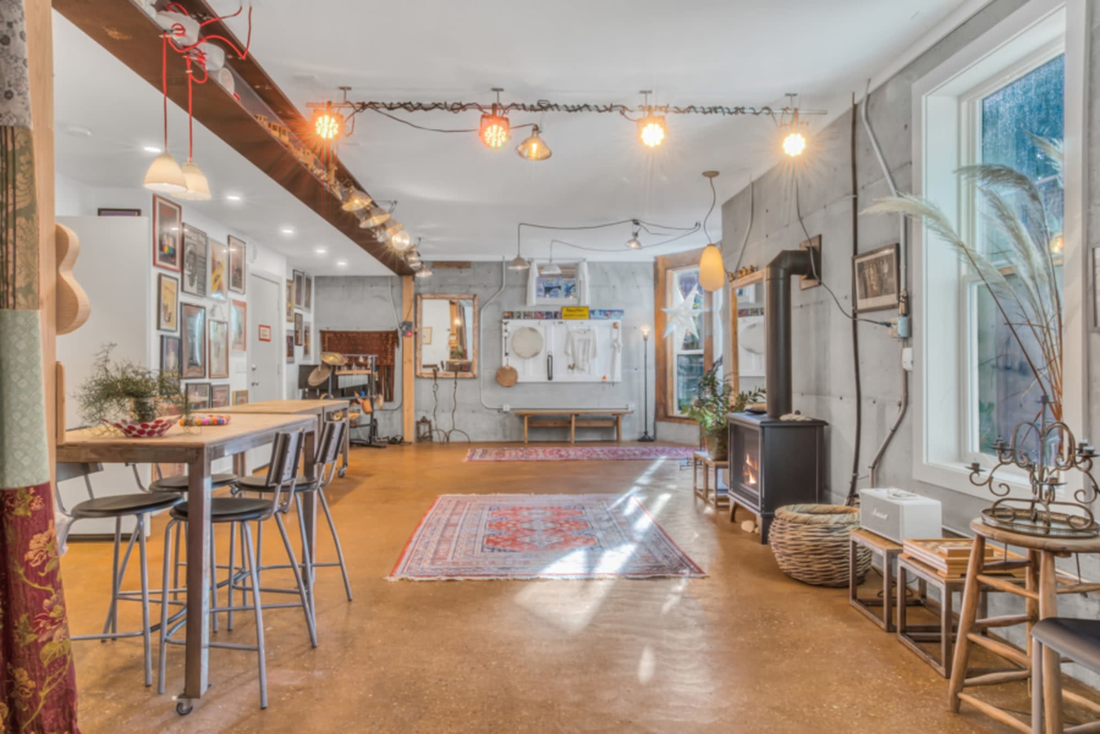 A spacious interior with concrete walls, a mixed lighting setup, and various decorations including rugs and artwork on the walls.