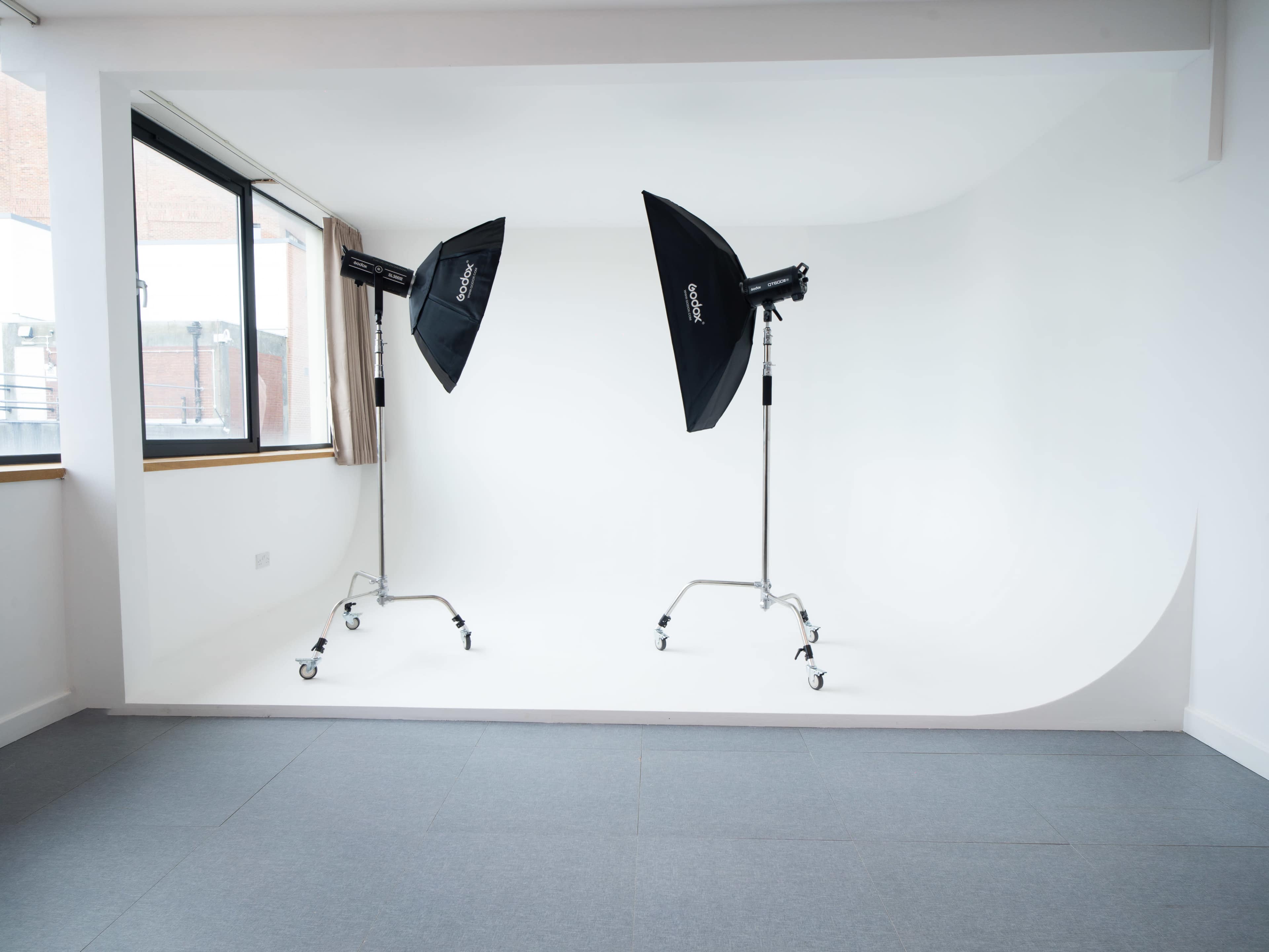 The image shows a well-lit photography studio with two softbox lights positioned on rolling stands, set against a plain white backdrop.
