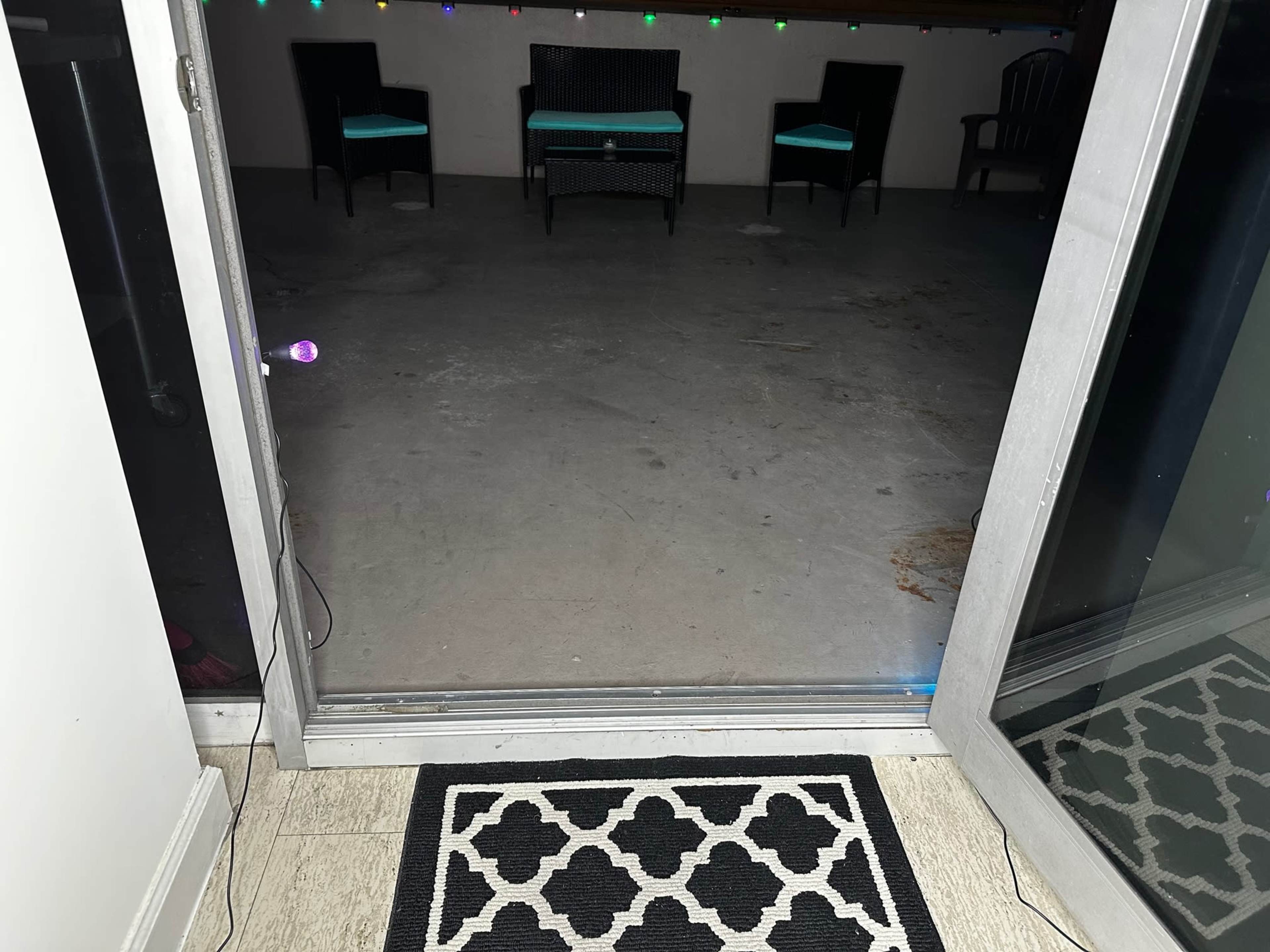 An open door leading to a dimly lit patio area with two chairs and a colorful light decoration along the wall.