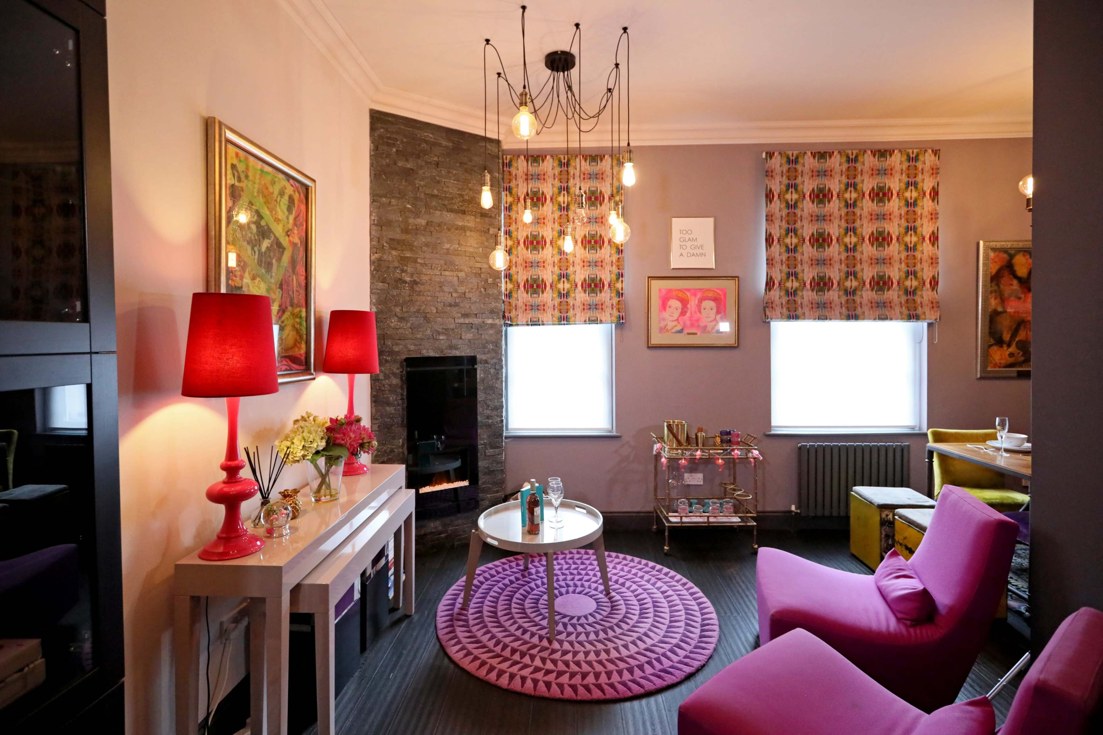 A cozy living room features pink furniture, a round carpet, decorative lights, and colorful artwork on the walls.