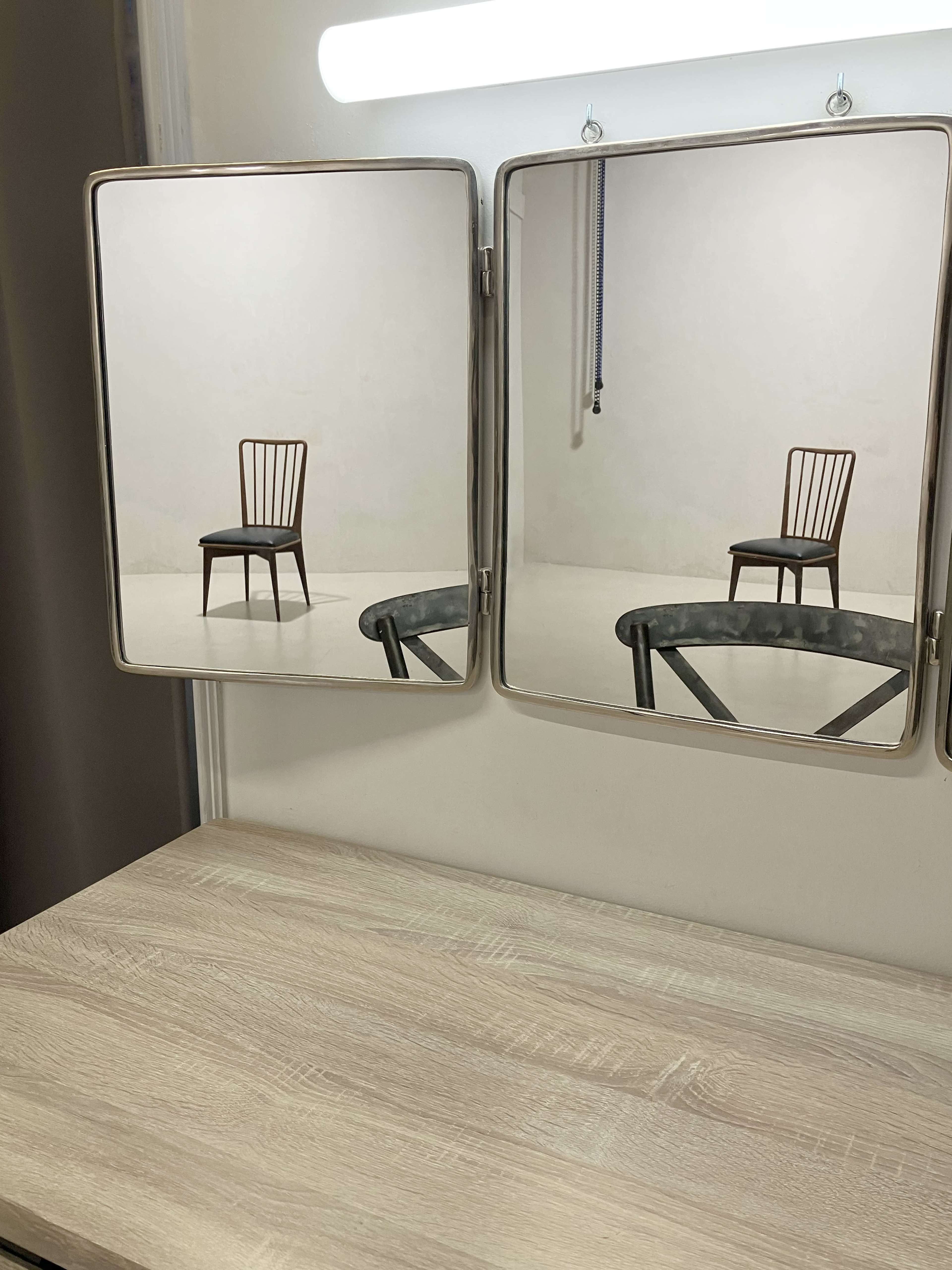 A wooden chair reflected in two mirrors mounted on a wall above a wooden surface.