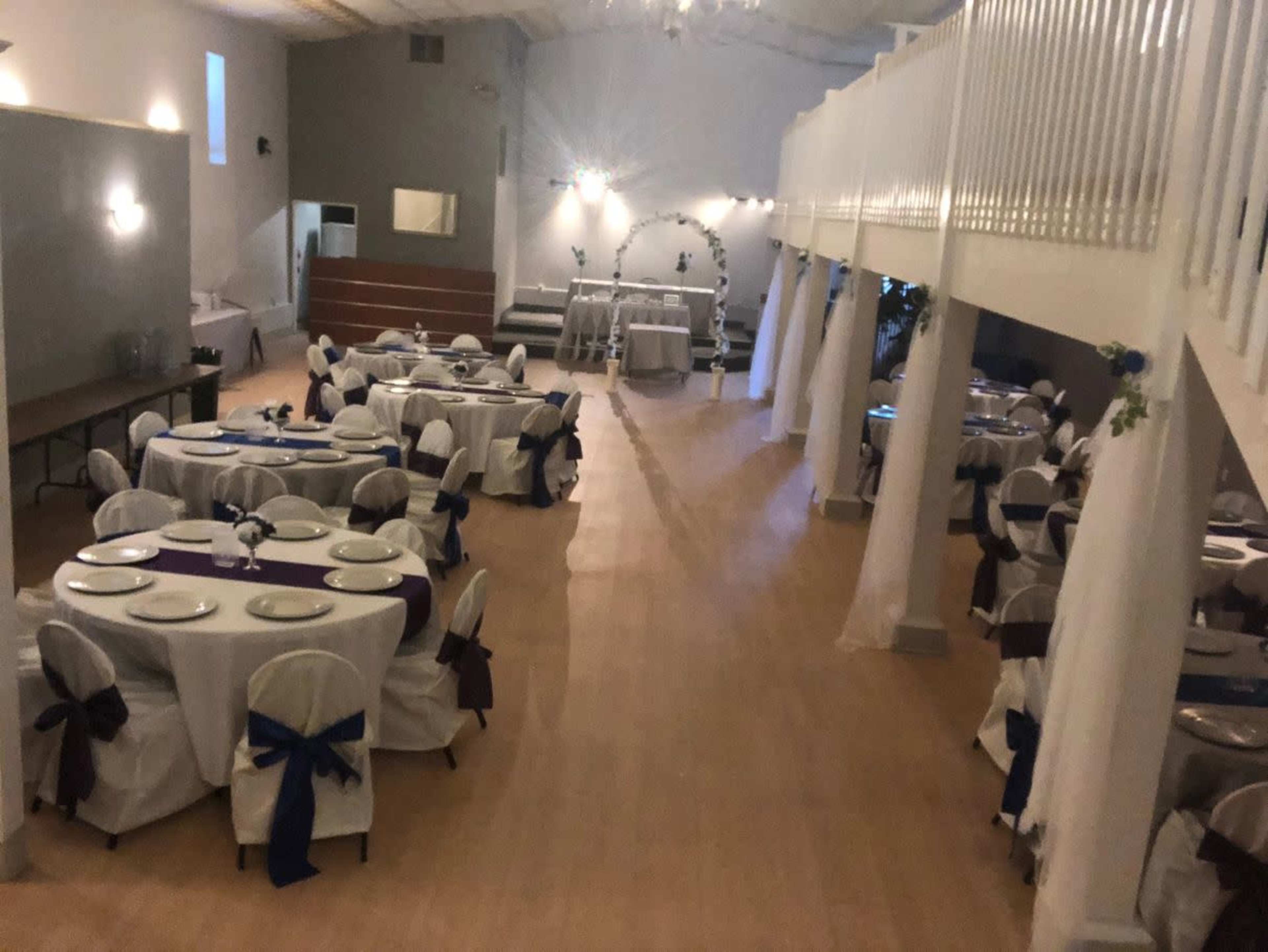 The image shows a banquet hall arranged with round tables covered in white tablecloths and decorated with blue and purple accents.