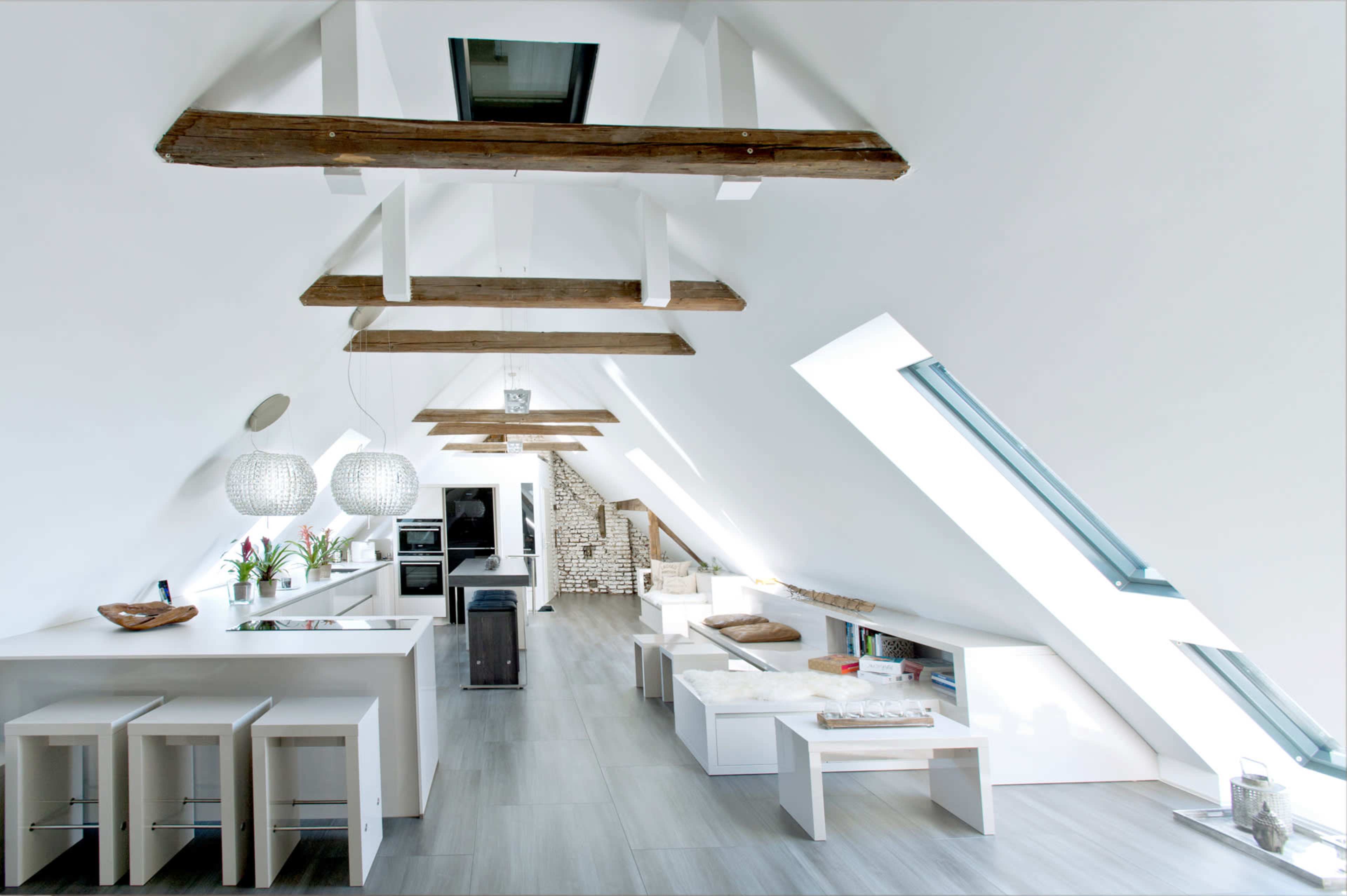 The image depicts a modern, minimalist attic space with wooden beams, a kitchen area, and a cozy seating arrangement.