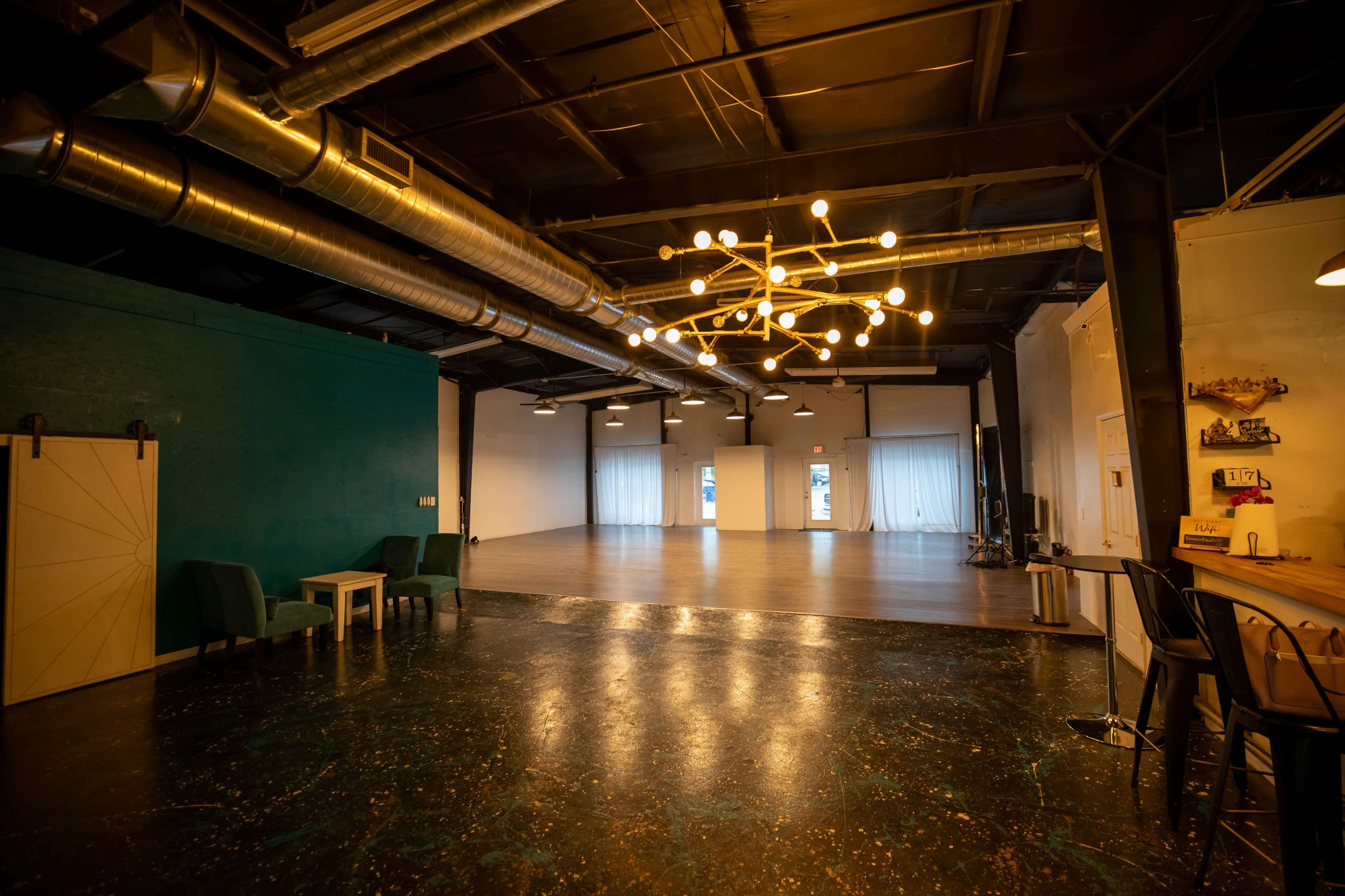 The image shows a spacious interior with a blue accent wall, modern lighting, and a mix of seating and open floor space.