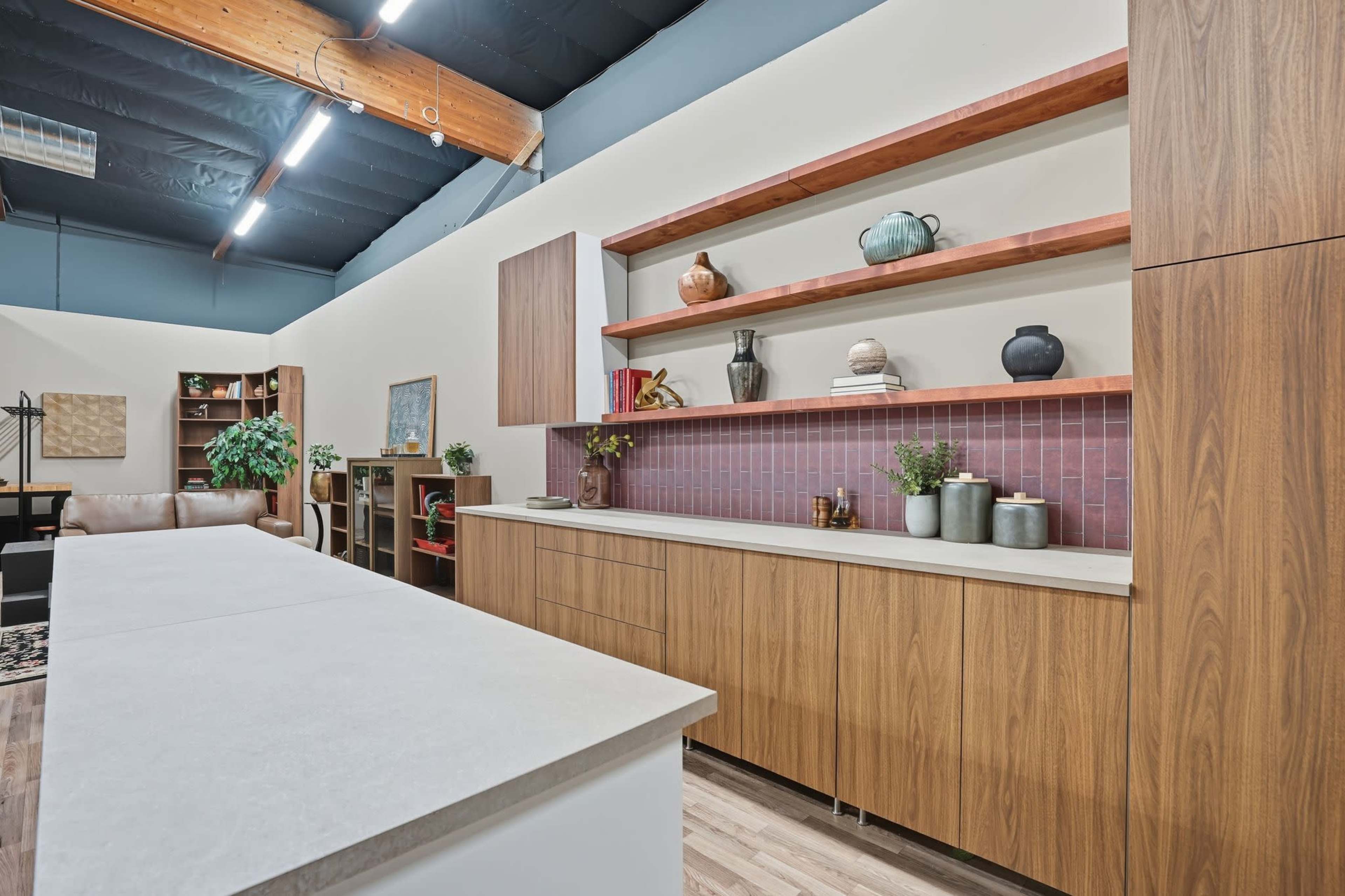 The image shows a modern kitchen with wooden cabinetry, open shelves displaying decorative vases, and a central island with a light-colored countertop.