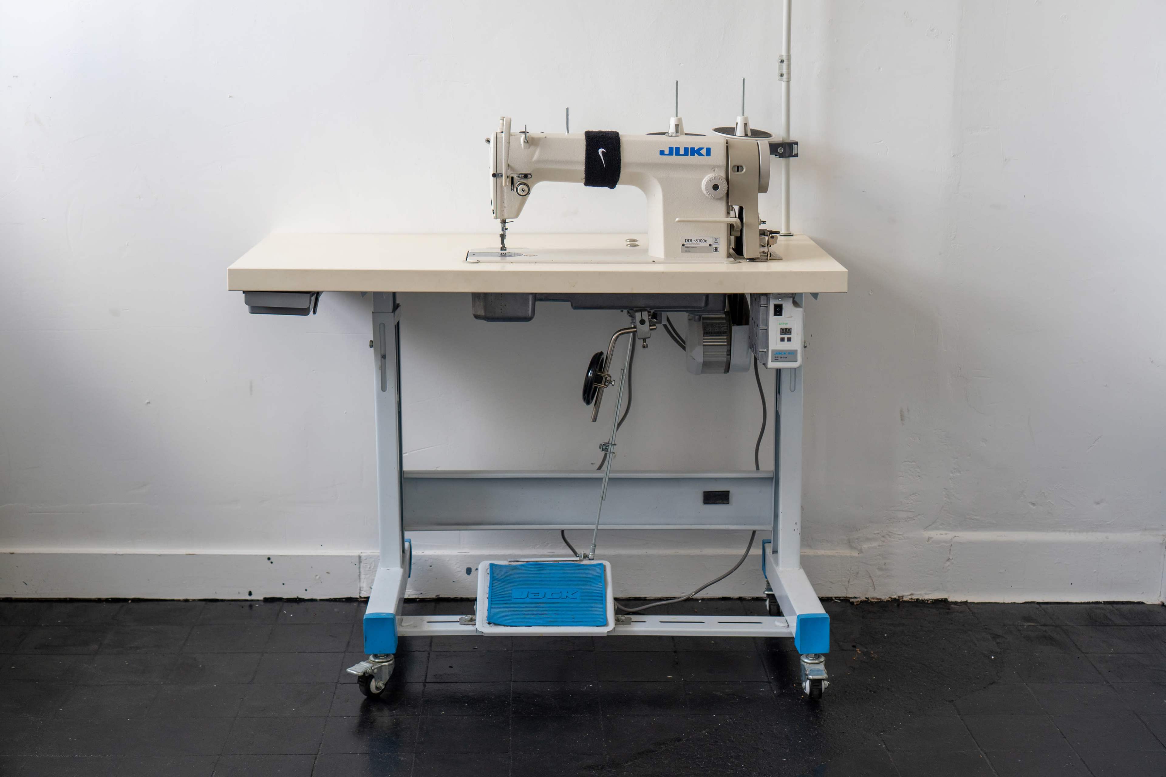 The image shows a Juki sewing machine set on a functional worktable with wheels in a minimally decorated room.