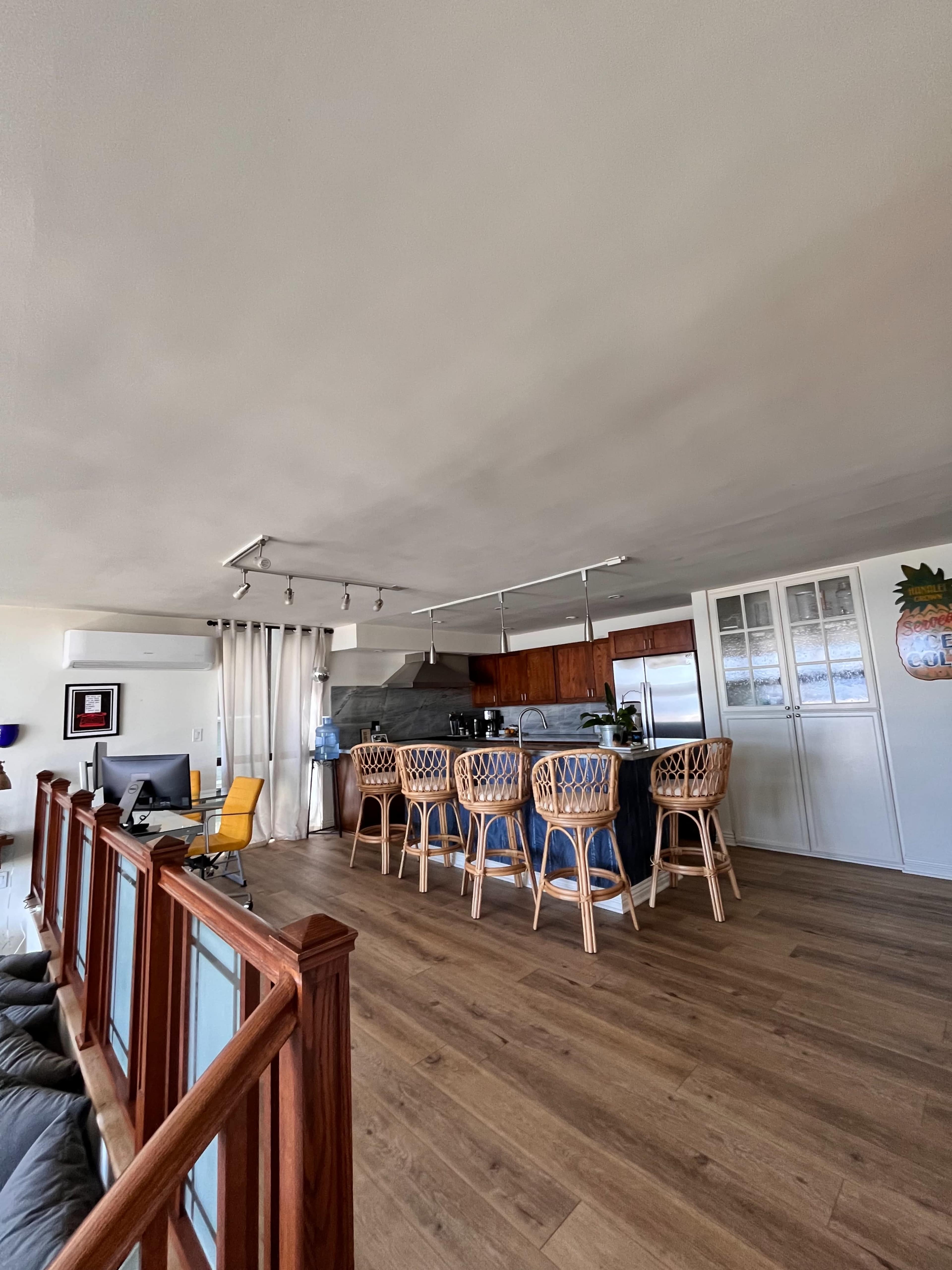 A modern kitchen and living area with a large island bar, wooden flooring, and a seating area with a yellow chair.