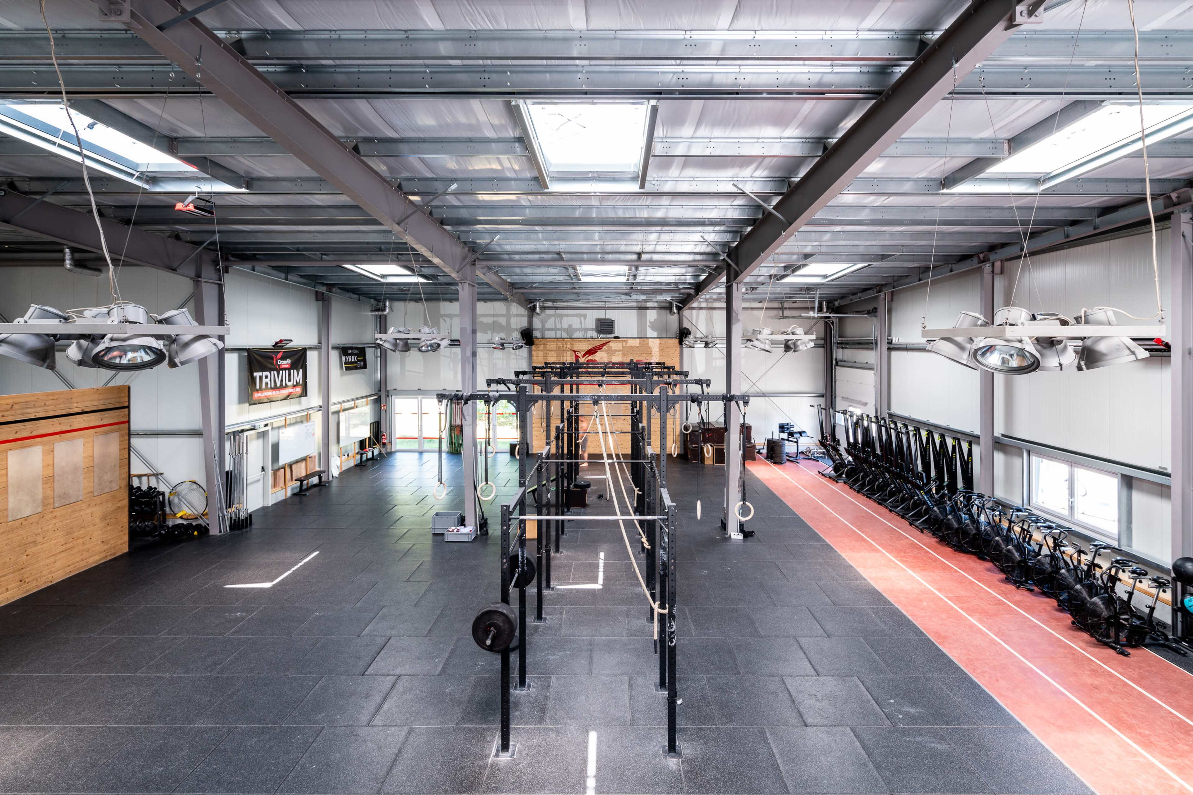 A spacious indoor gym with a central area for weightlifting and rows of rowing machines along one side.