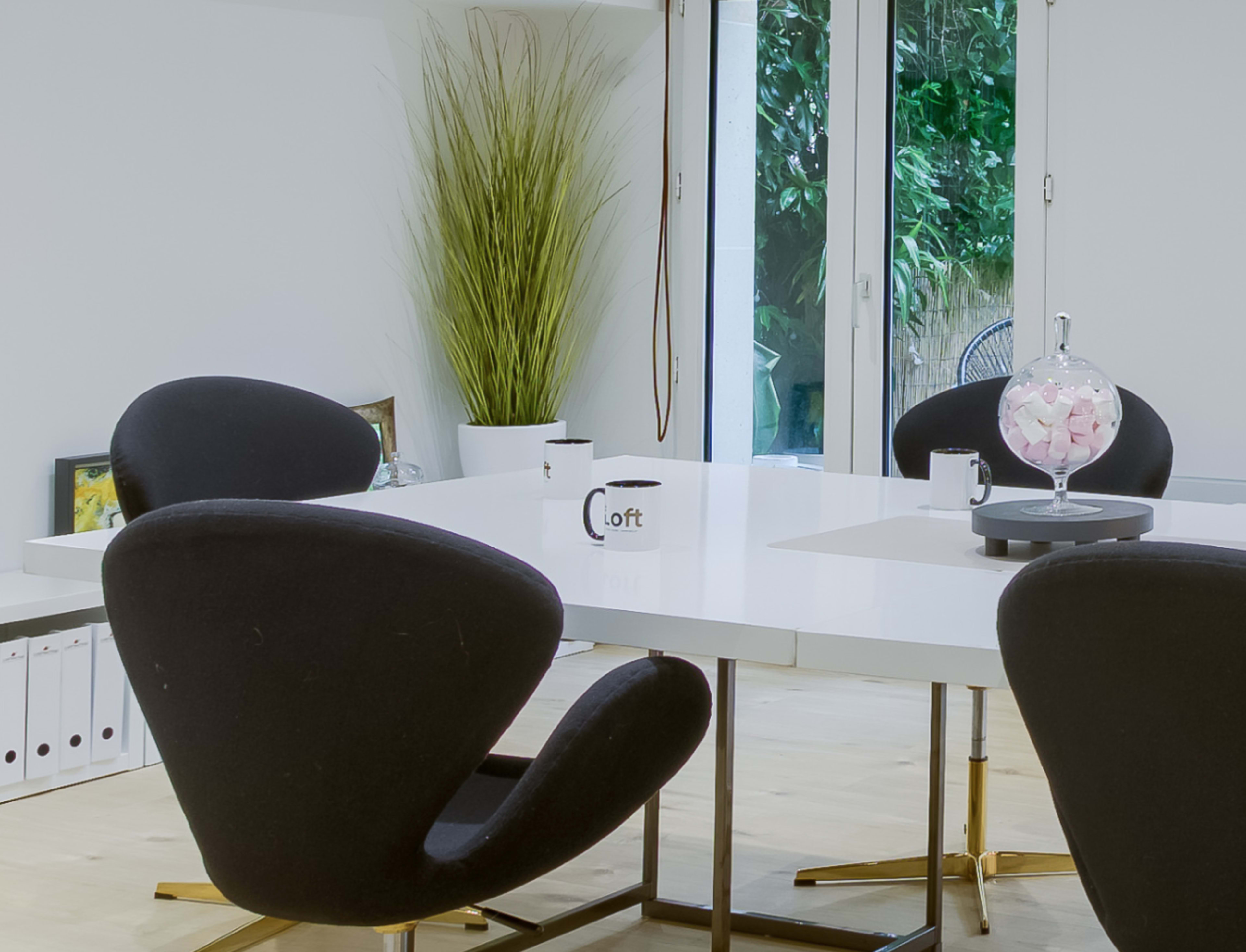 A modern meeting room features a white table surrounded by black chairs, with a decorative plant and glass orb centerpiece on display.