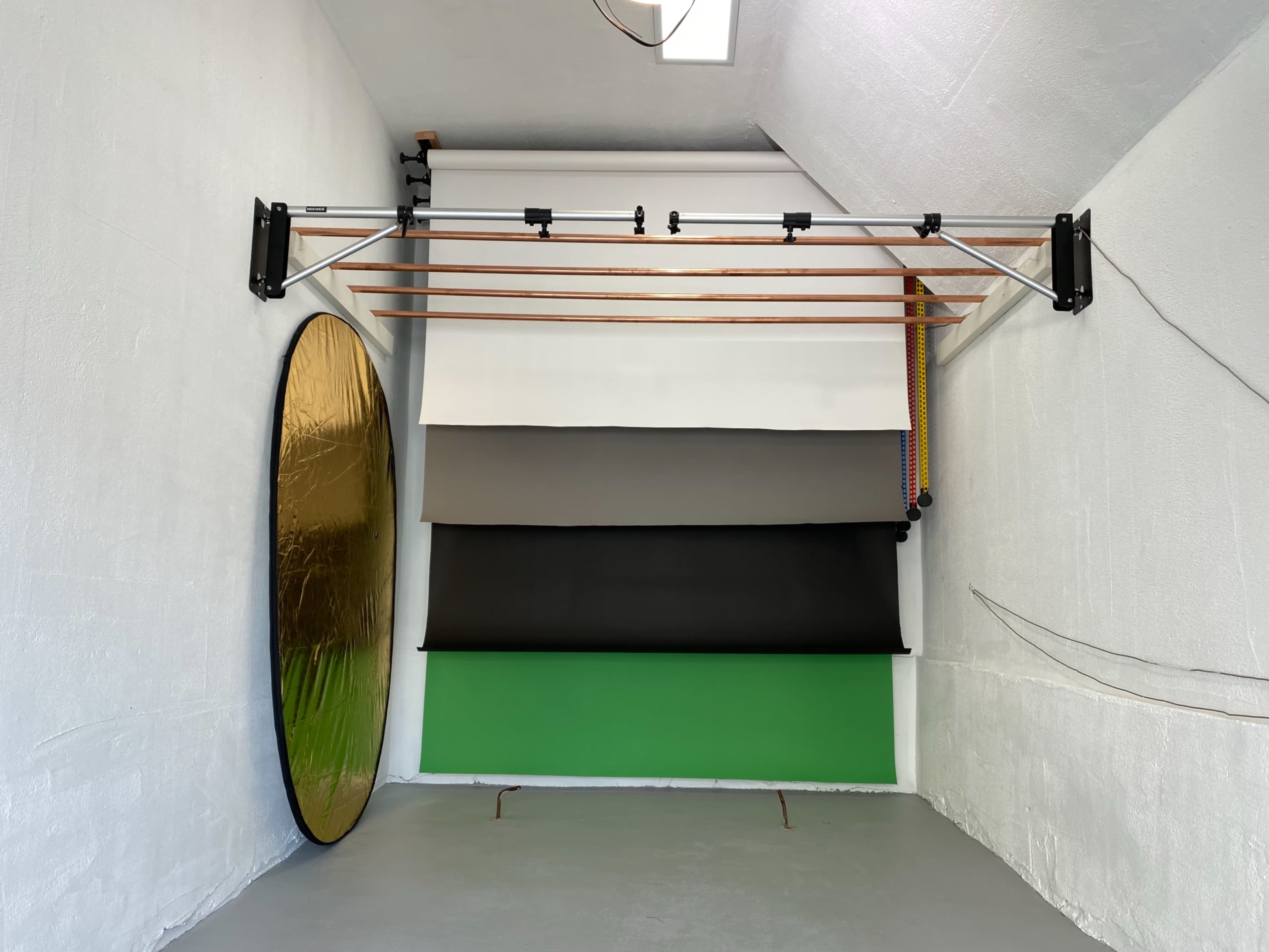 A photography studio with a backdrop stand holding several color backdrop rolls and a round reflector mounted on the wall.