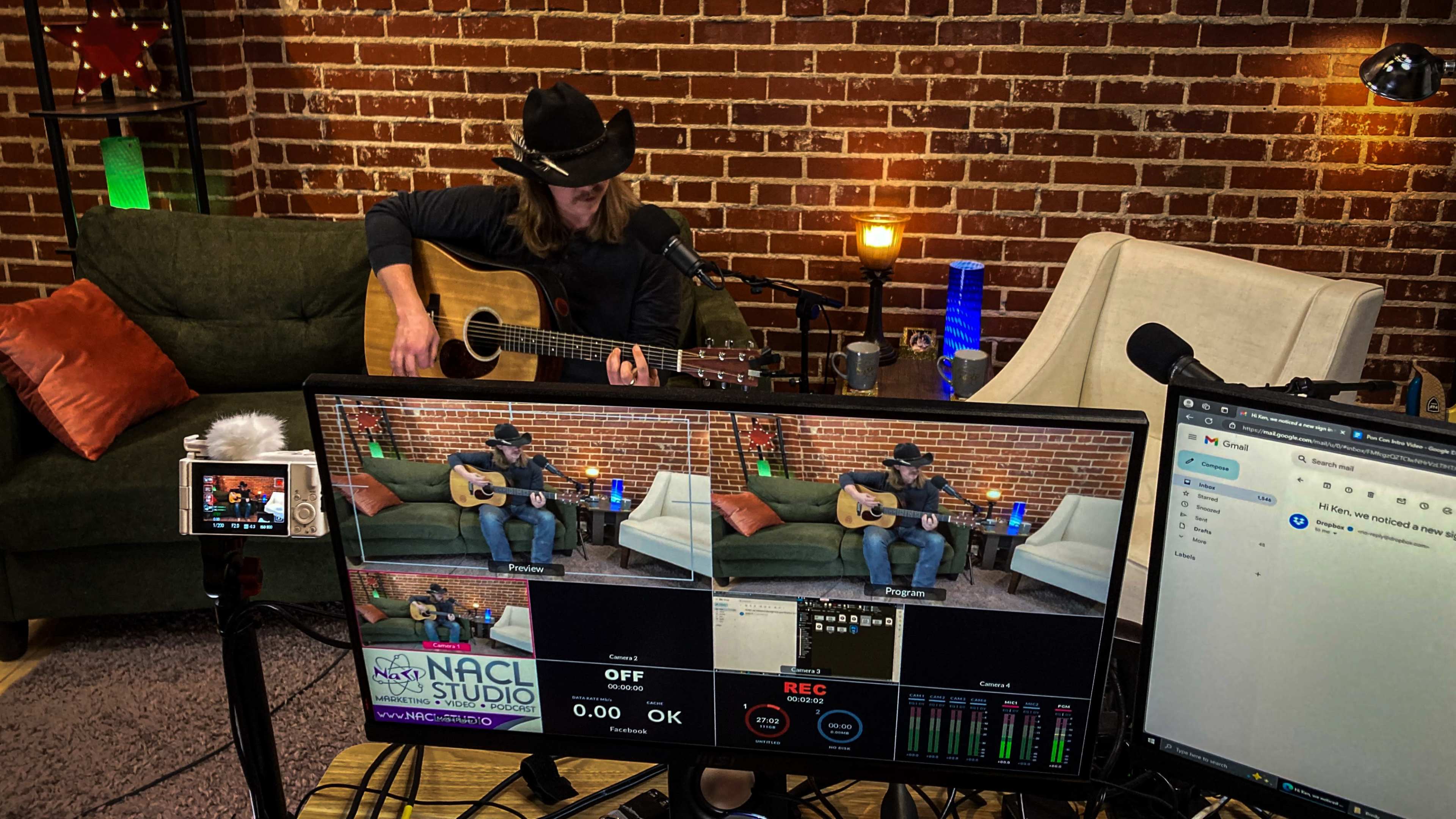 A musician is playing an acoustic guitar in a studio setting, with cameras and a mixing console capturing the performance.