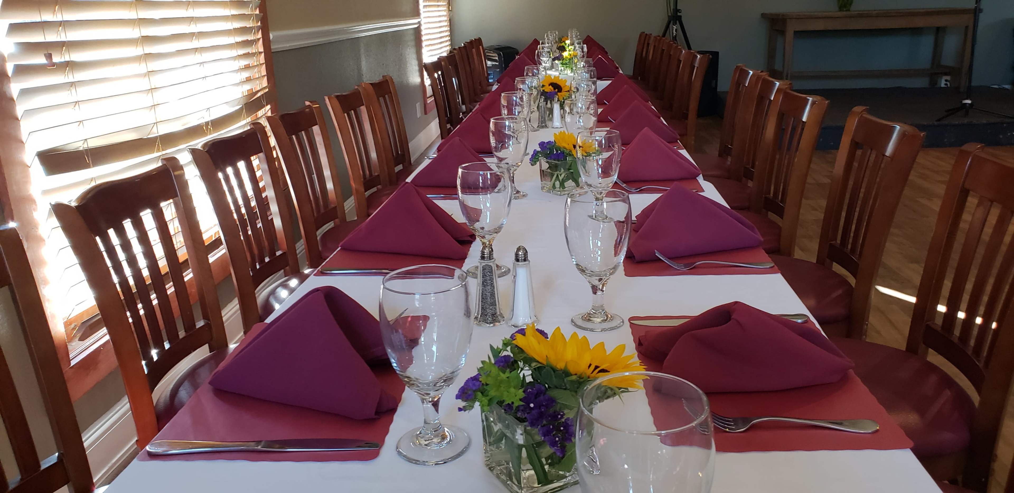 A long dining table is set with glasses, silverware, and folded napkins, adorned with floral centerpieces and a white tablecloth.