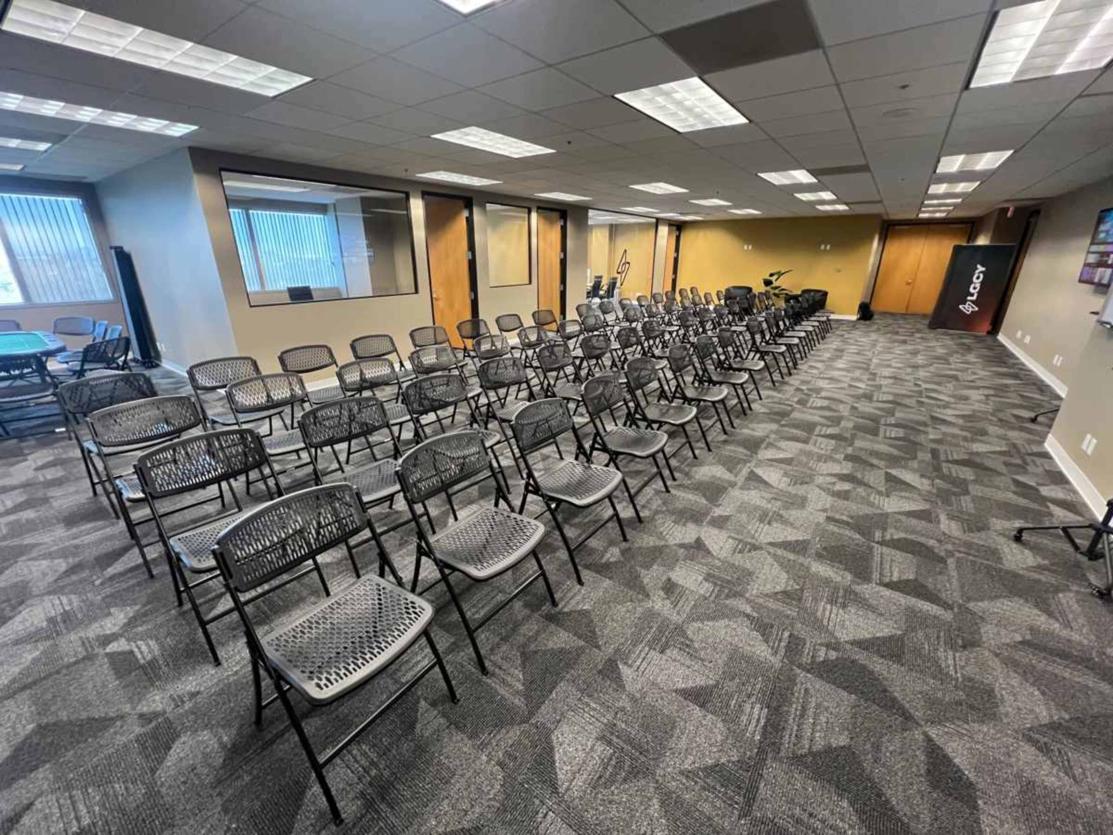 The image shows a room arranged with rows of black folding chairs, set up for an event or meeting.
