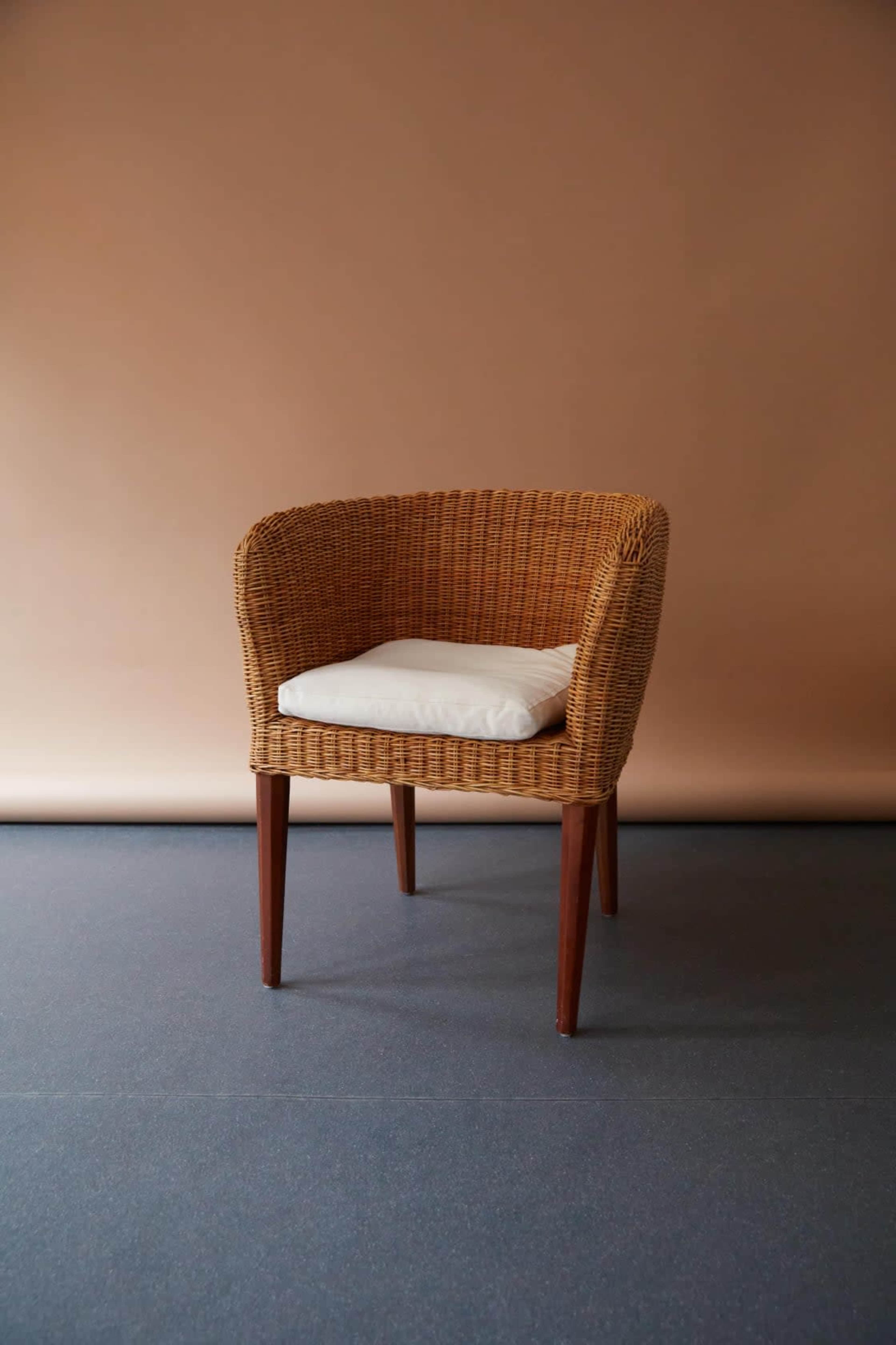 A woven wicker chair with a white cushion is positioned against a beige background.