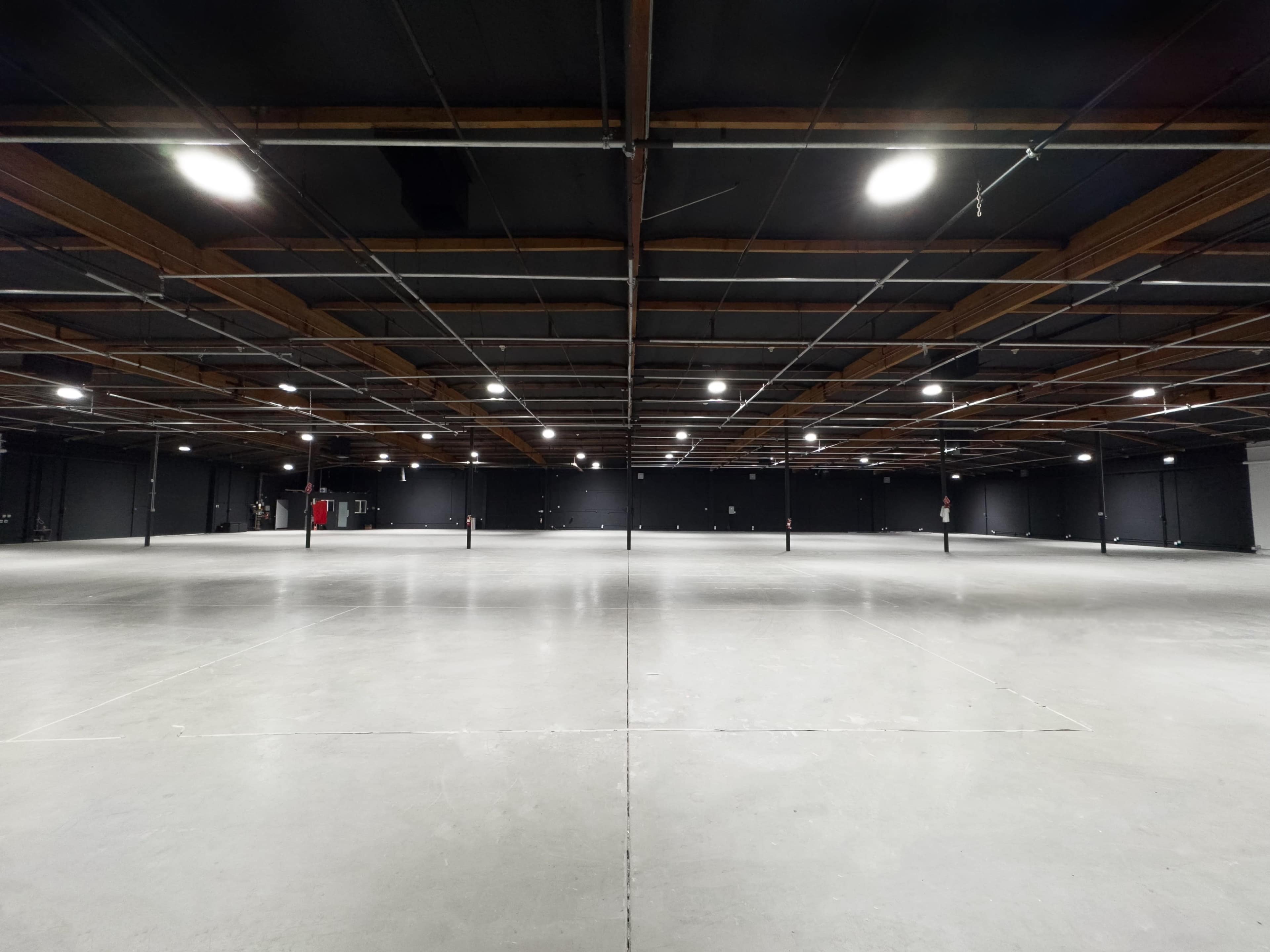 A large, empty warehouse space with polished concrete floors and exposed wooden beams overhead.
