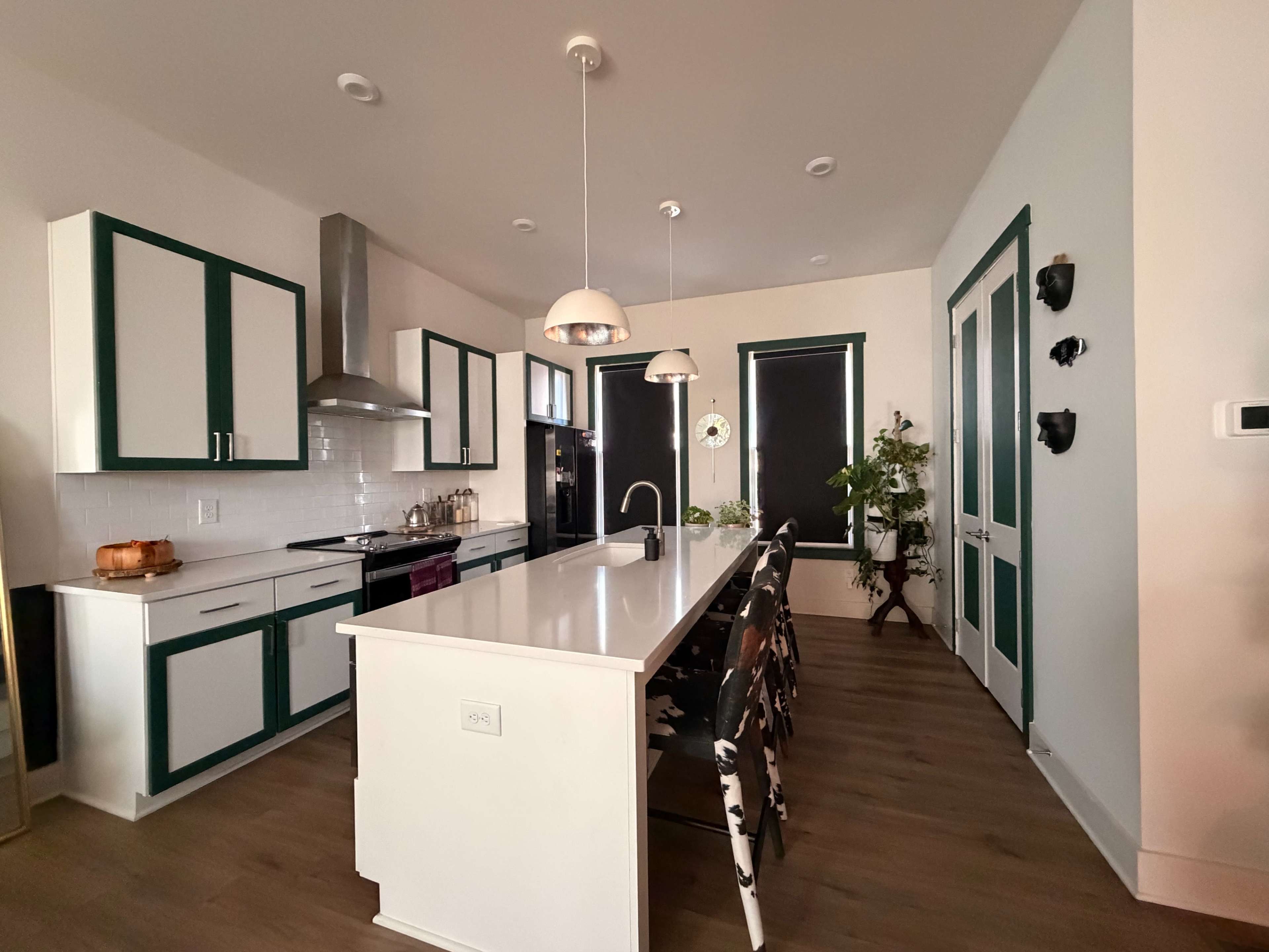 The image shows a modern kitchen with a central island, green-trimmed cabinetry, and adjustable pendant lighting.