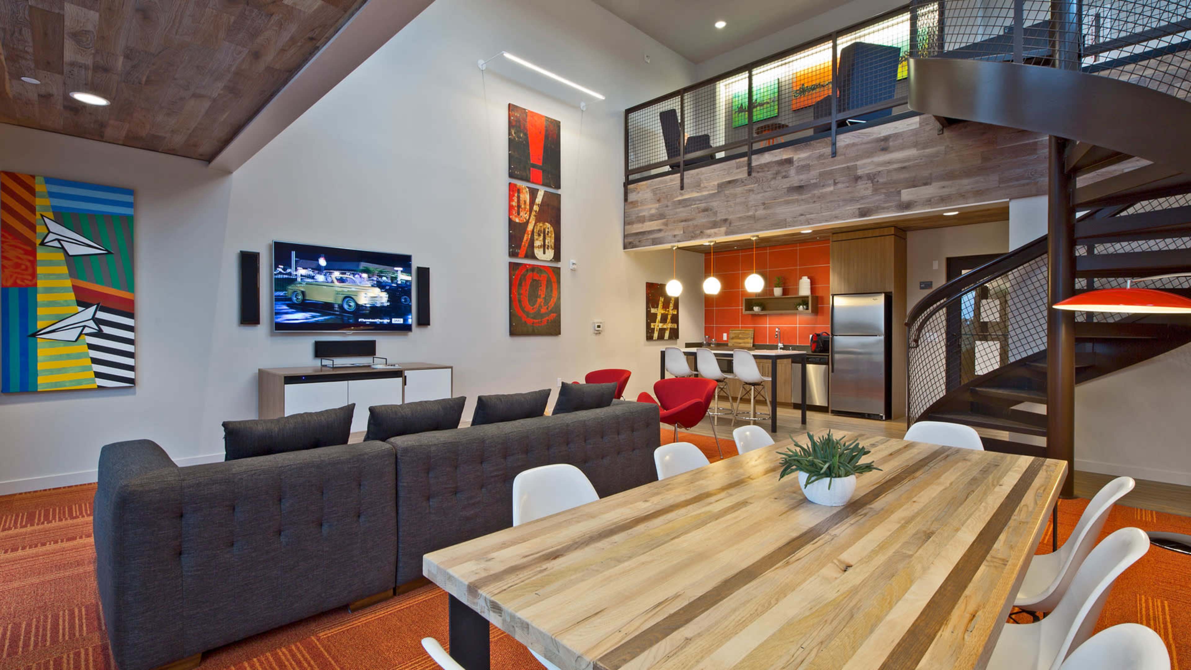 The image shows a modern, two-story living space featuring a dining table, a sectional sofa, a spiral staircase, and a wall-mounted television.