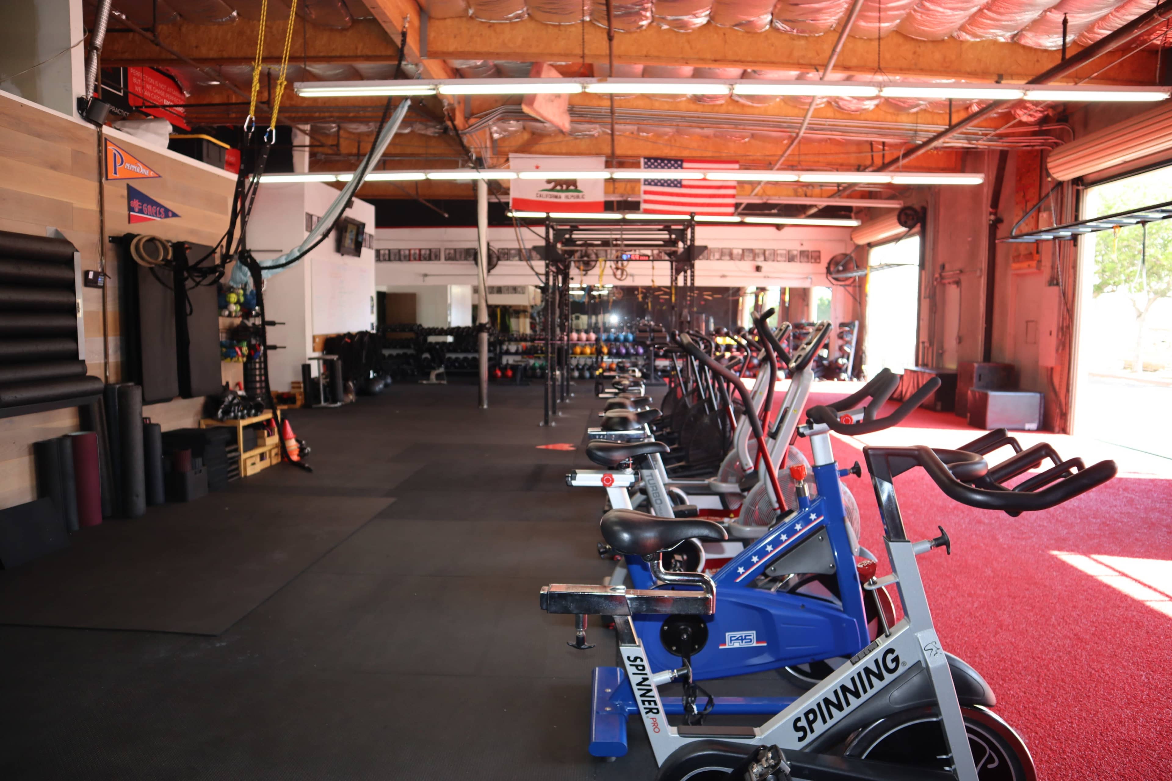 An indoor gym with rows of spinning bikes and various exercise equipment against a backdrop of a suspended American flag.