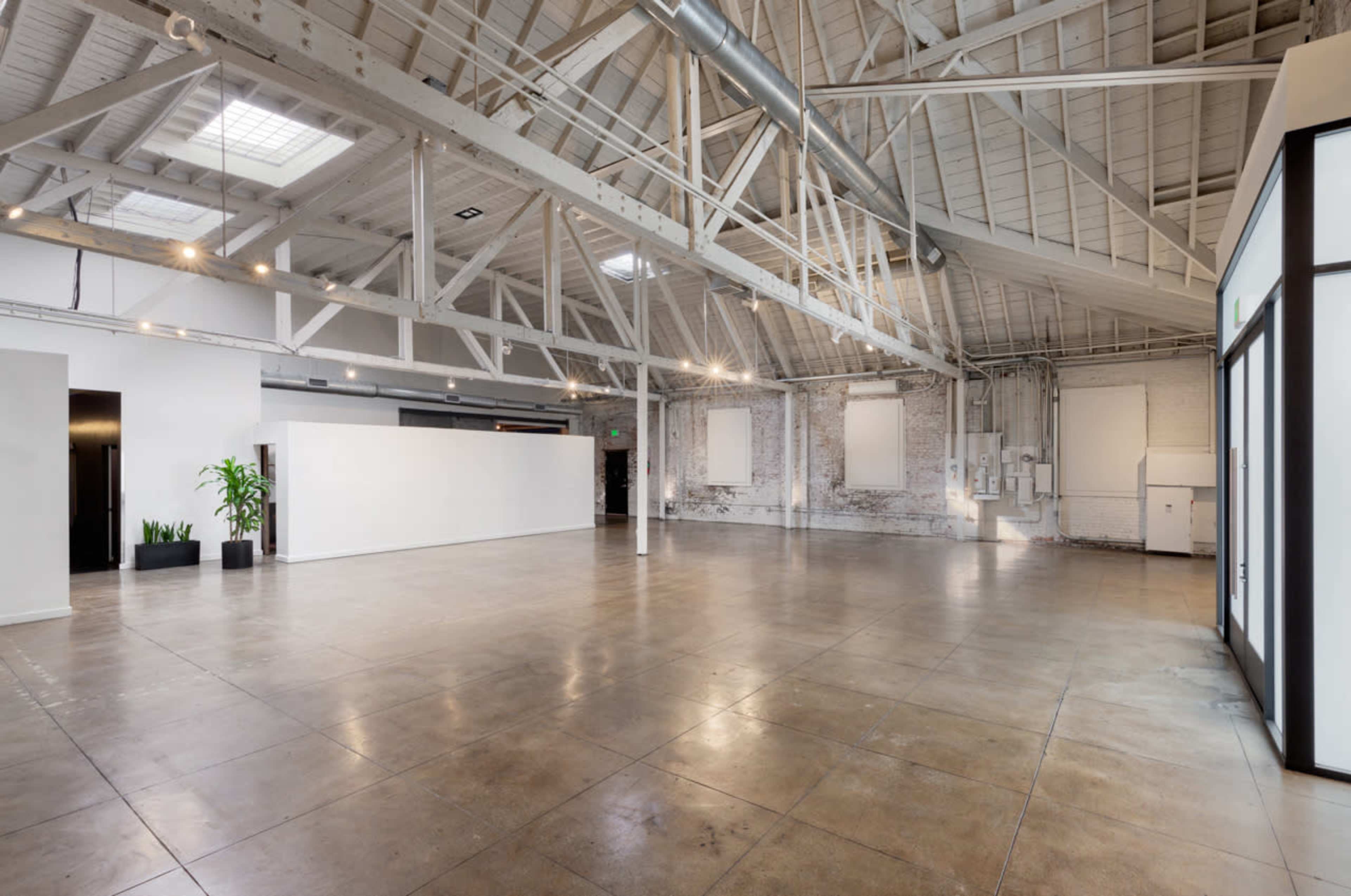 The image shows a spacious, industrial-style interior with high ceilings, exposed beams, and polished concrete floors.