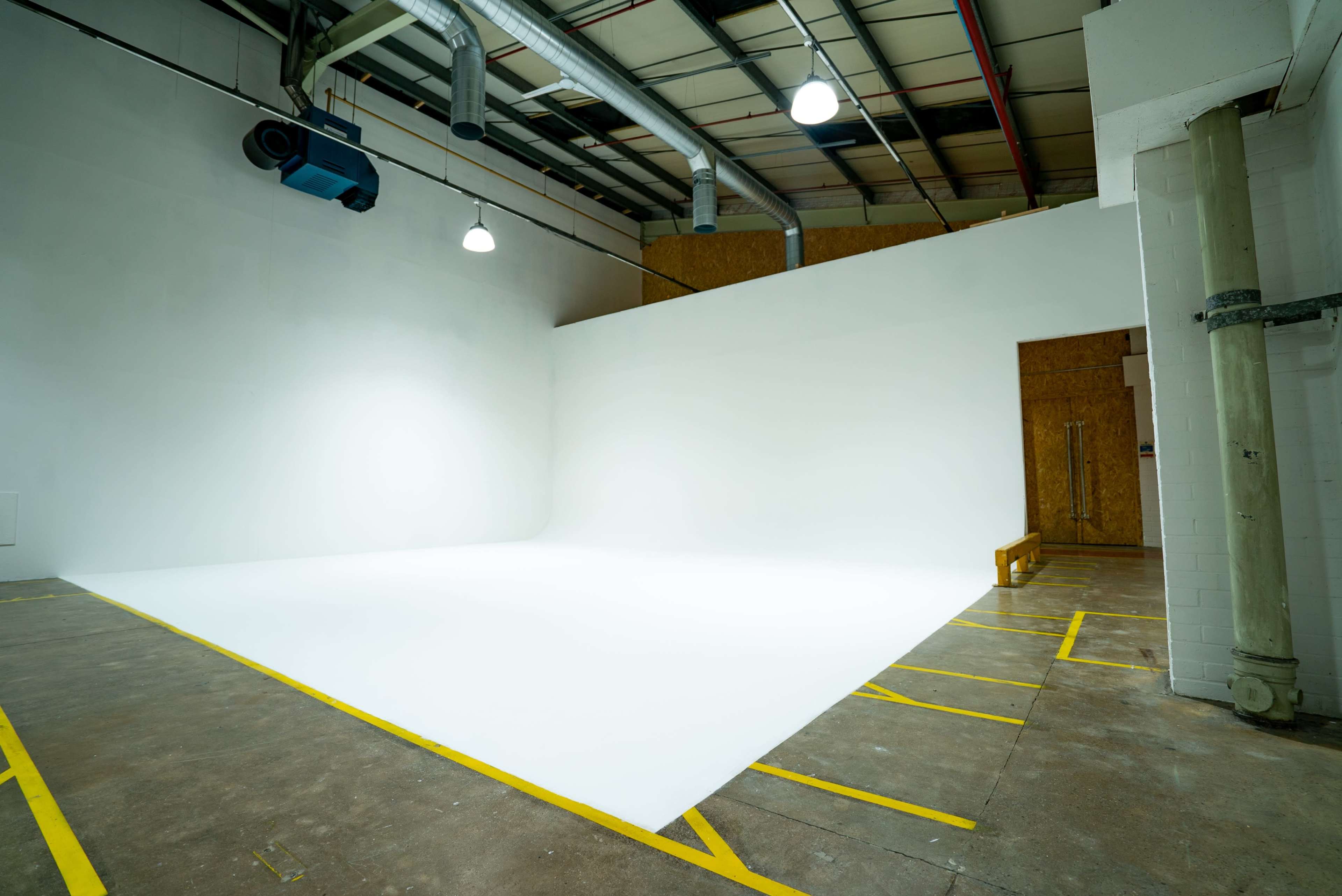 An empty photography studio features a seamless white backdrop, with overhead lights and exposed structural elements.