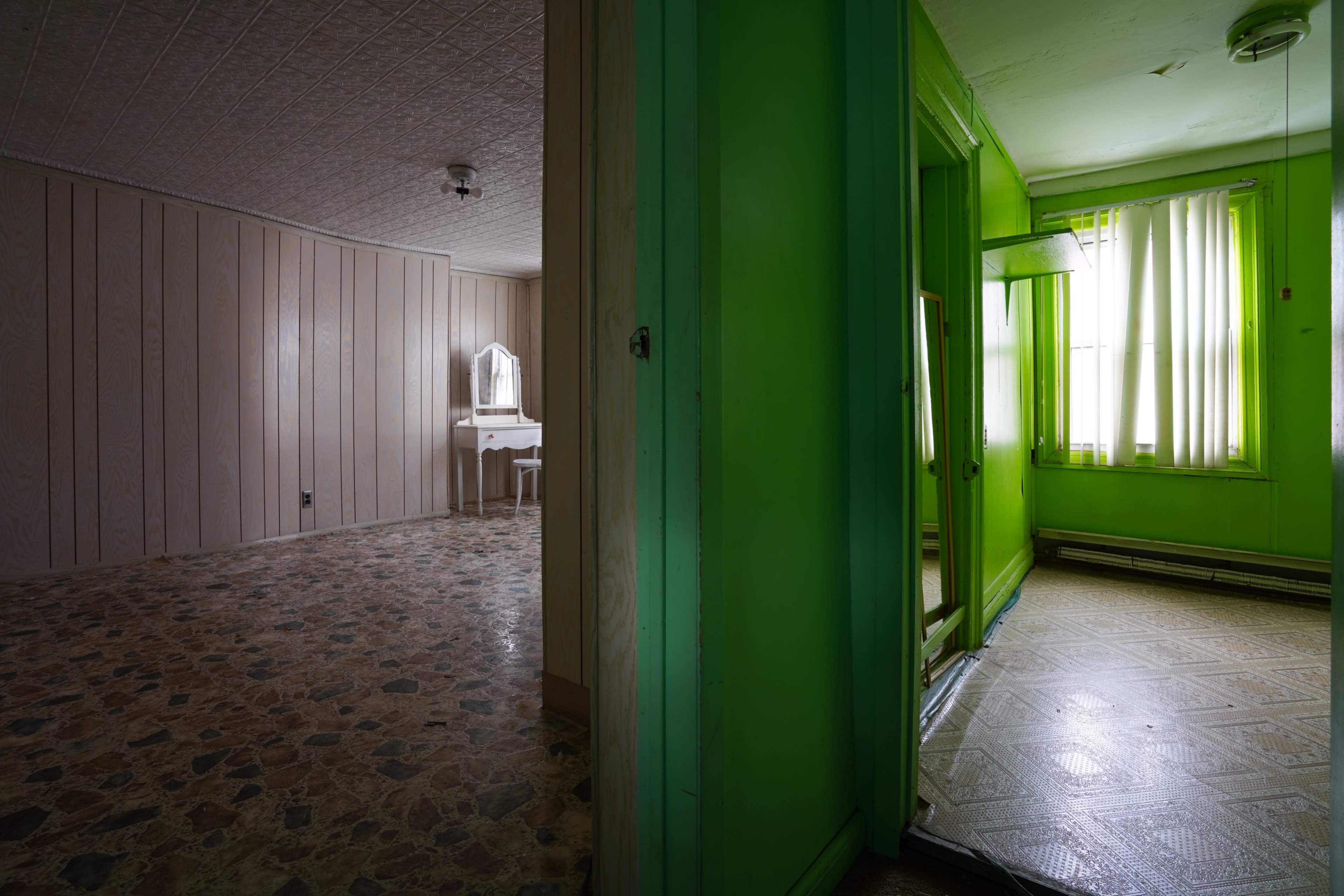 A vacant room featuring green walls, a vanity table, and a doorway leading to another area with patterned flooring.
