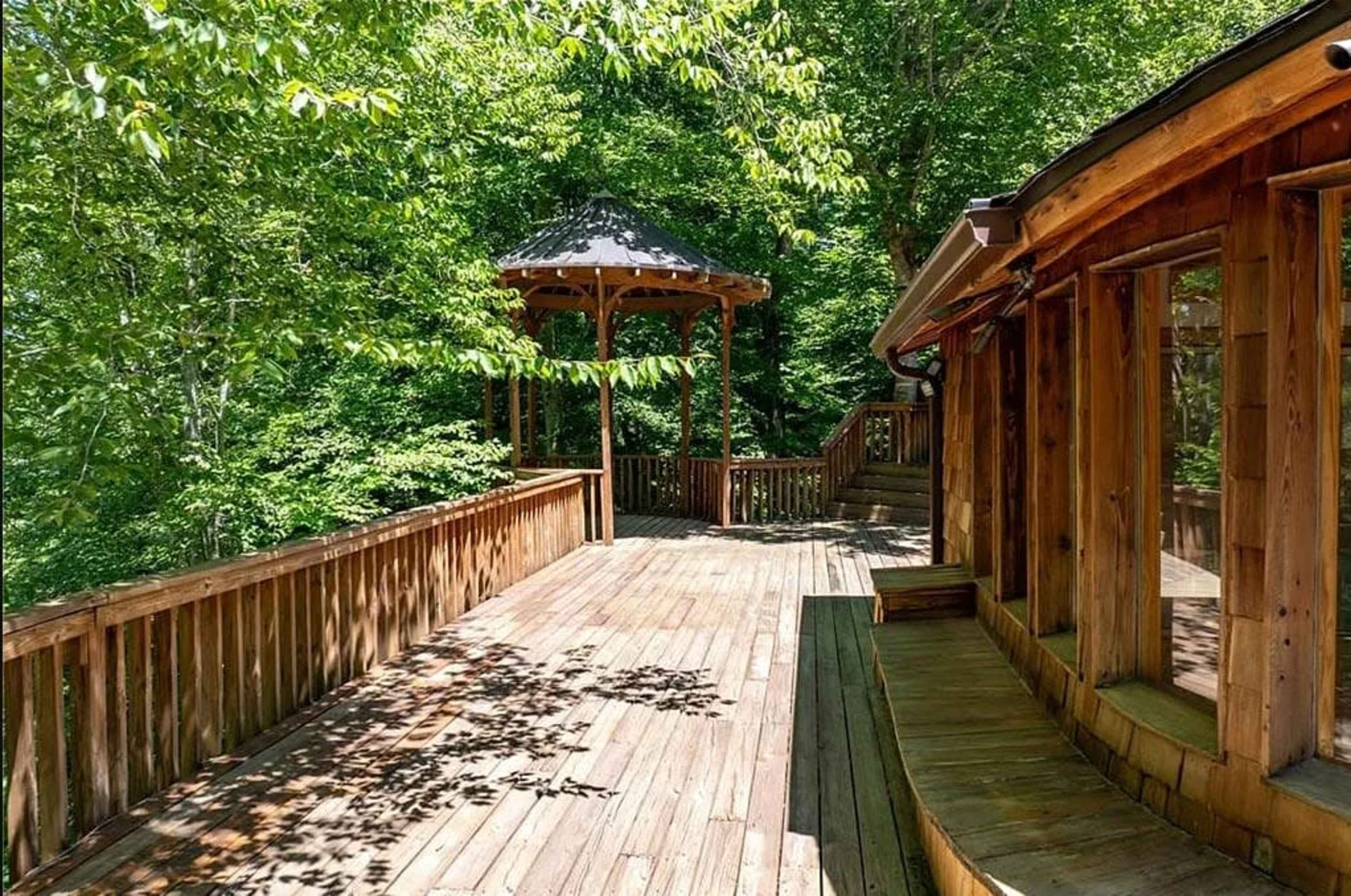 The image depicts a wooden deck surrounded by dense greenery, featuring a gazebo at one end.