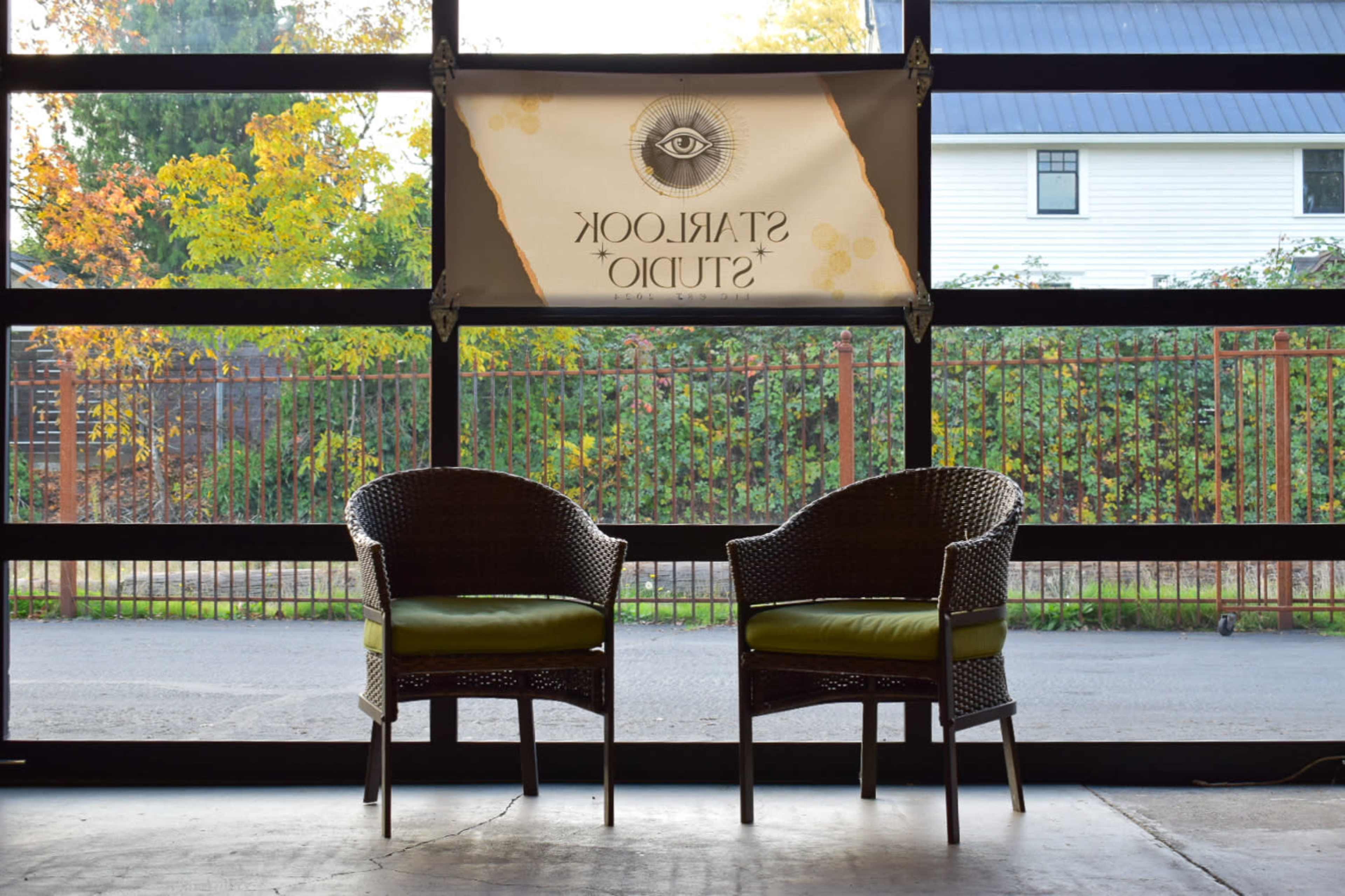 Two wicker chairs with green cushions are positioned in front of a large window displaying a banner for "Starlight Studio."