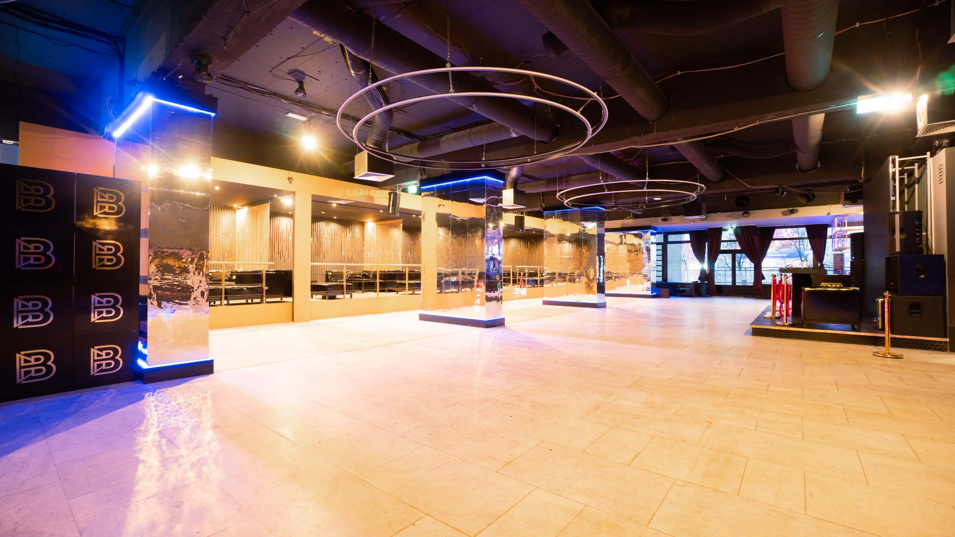 A spacious, modern interior of a venue with circular light fixtures and mirrored columns, designed for events or gatherings.