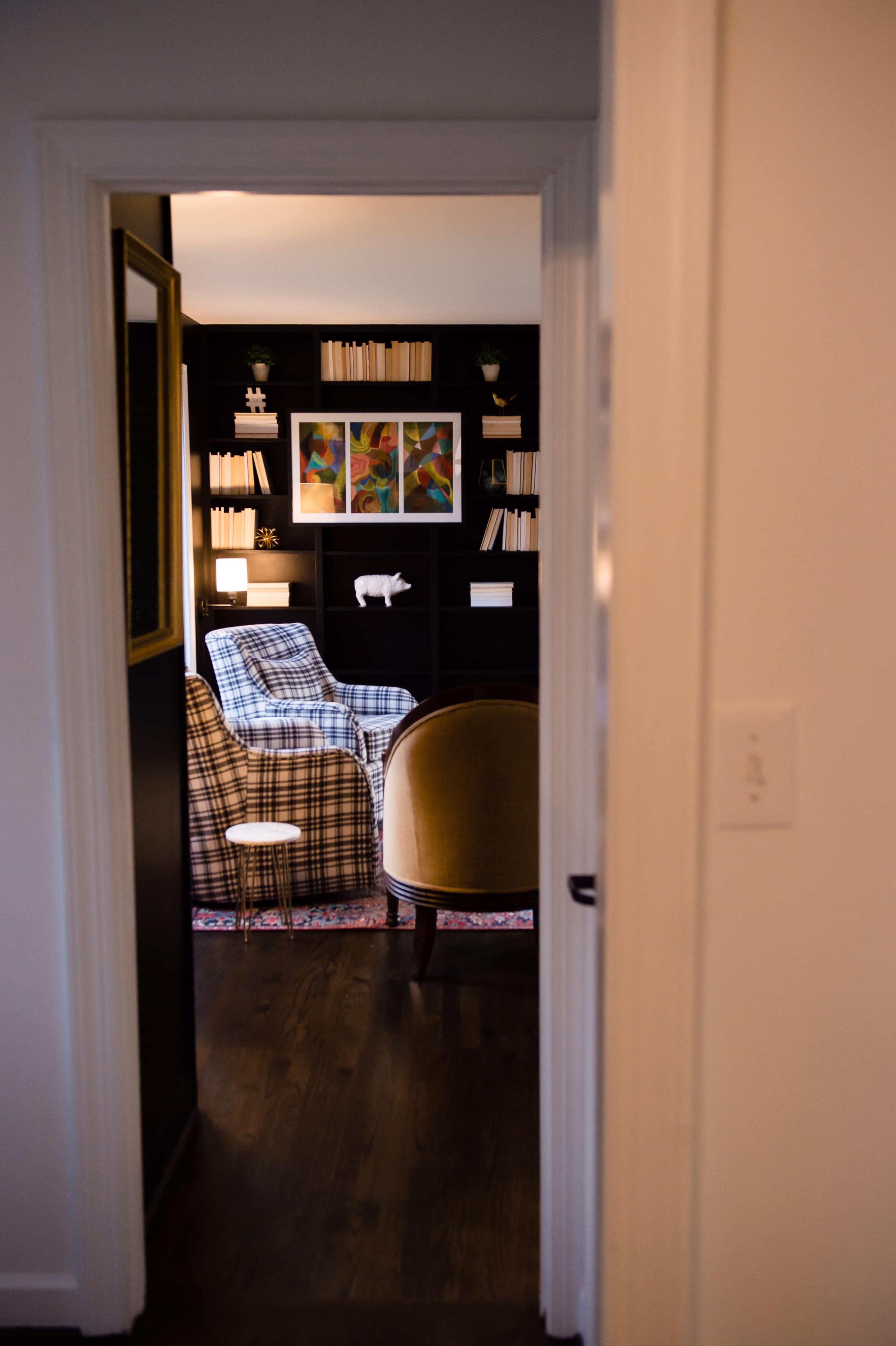 A glimpse through a doorway reveals a cozy sitting area with patterned chairs and shelves filled with books and artwork.