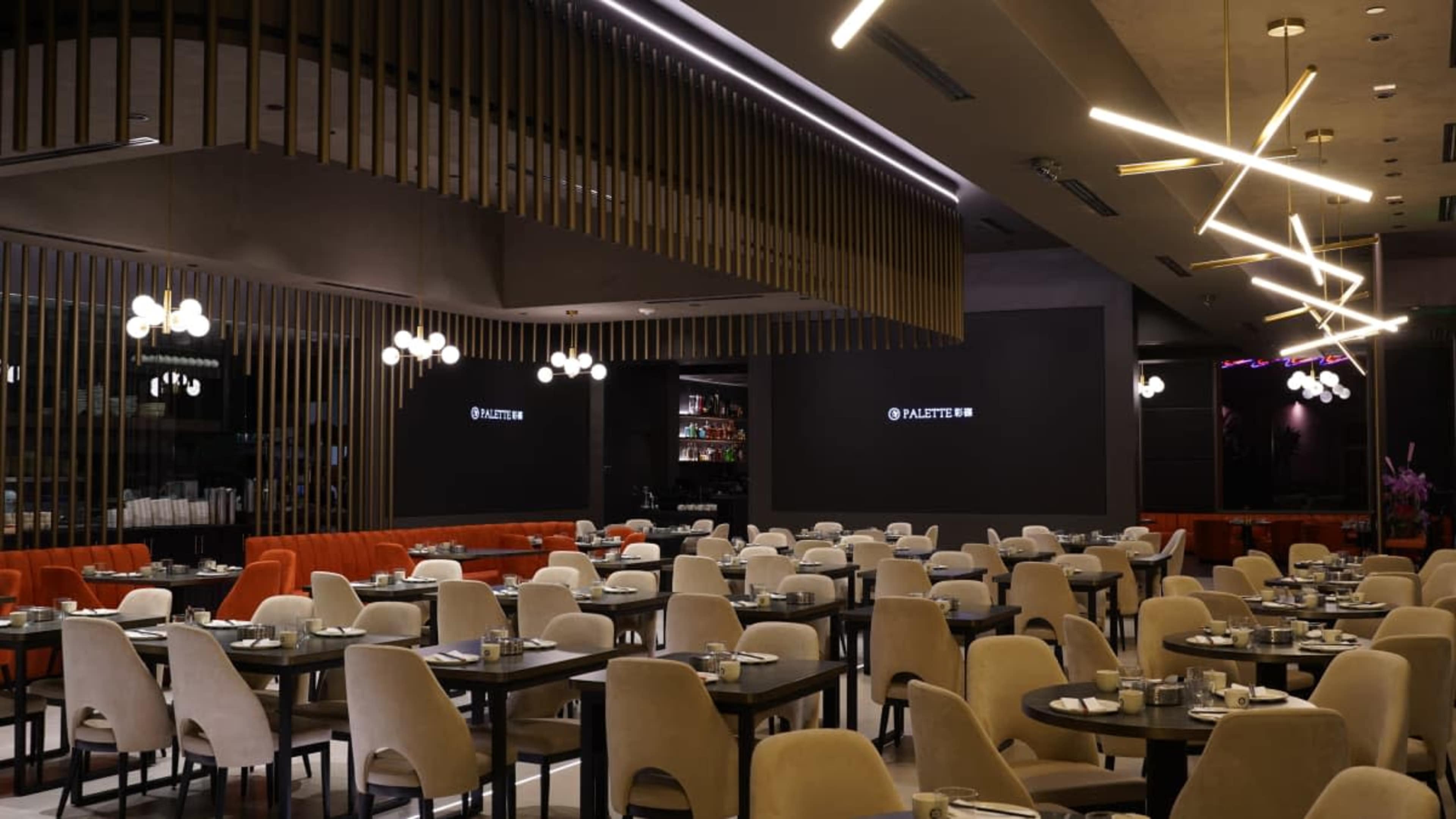 The image shows a modern restaurant interior featuring multiple tables and chairs, with a sleek bar at the back and contemporary lighting fixtures.