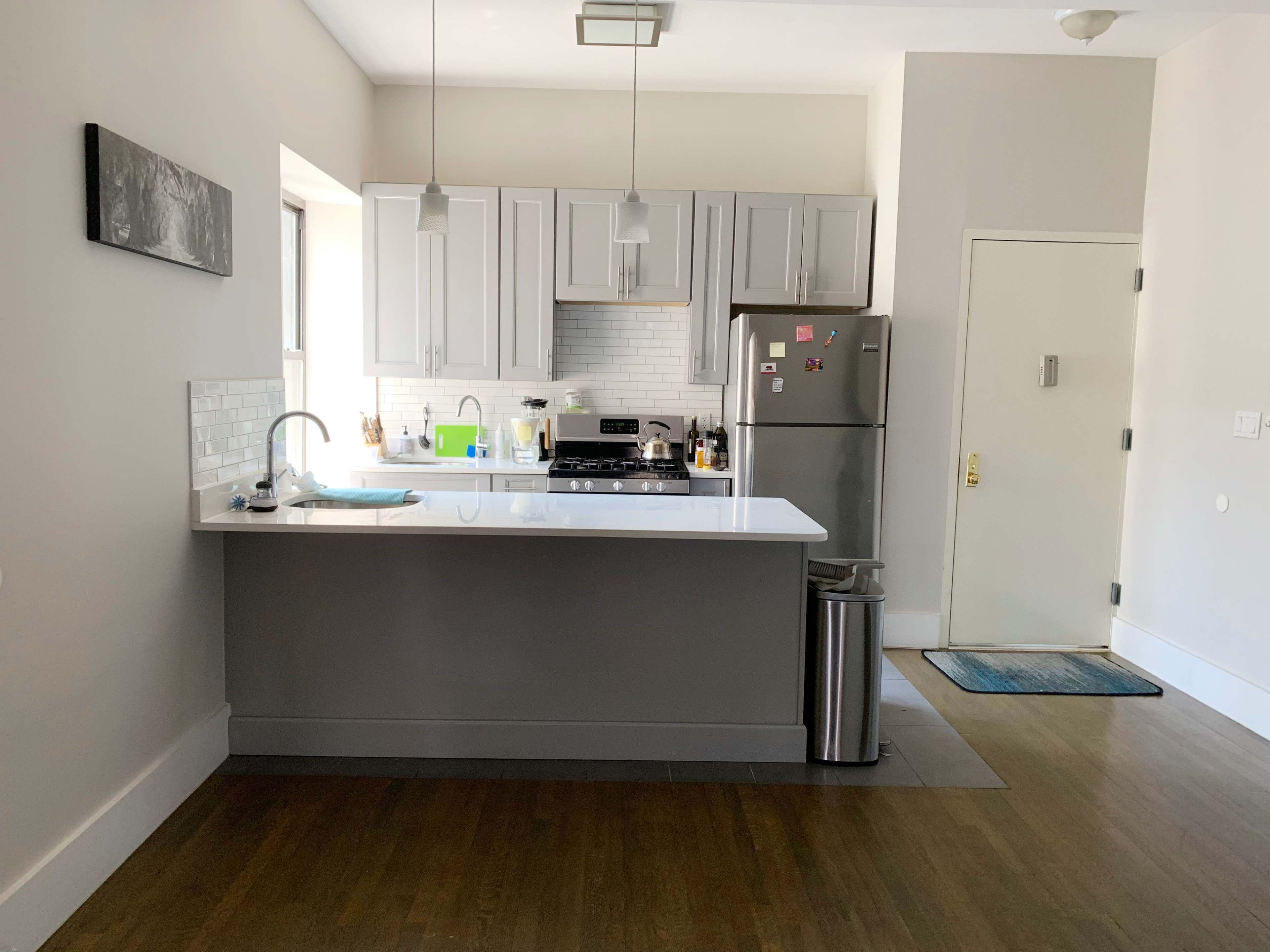 A modern kitchen with light gray cabinetry, a white countertop, a stainless steel refrigerator, and a side door.