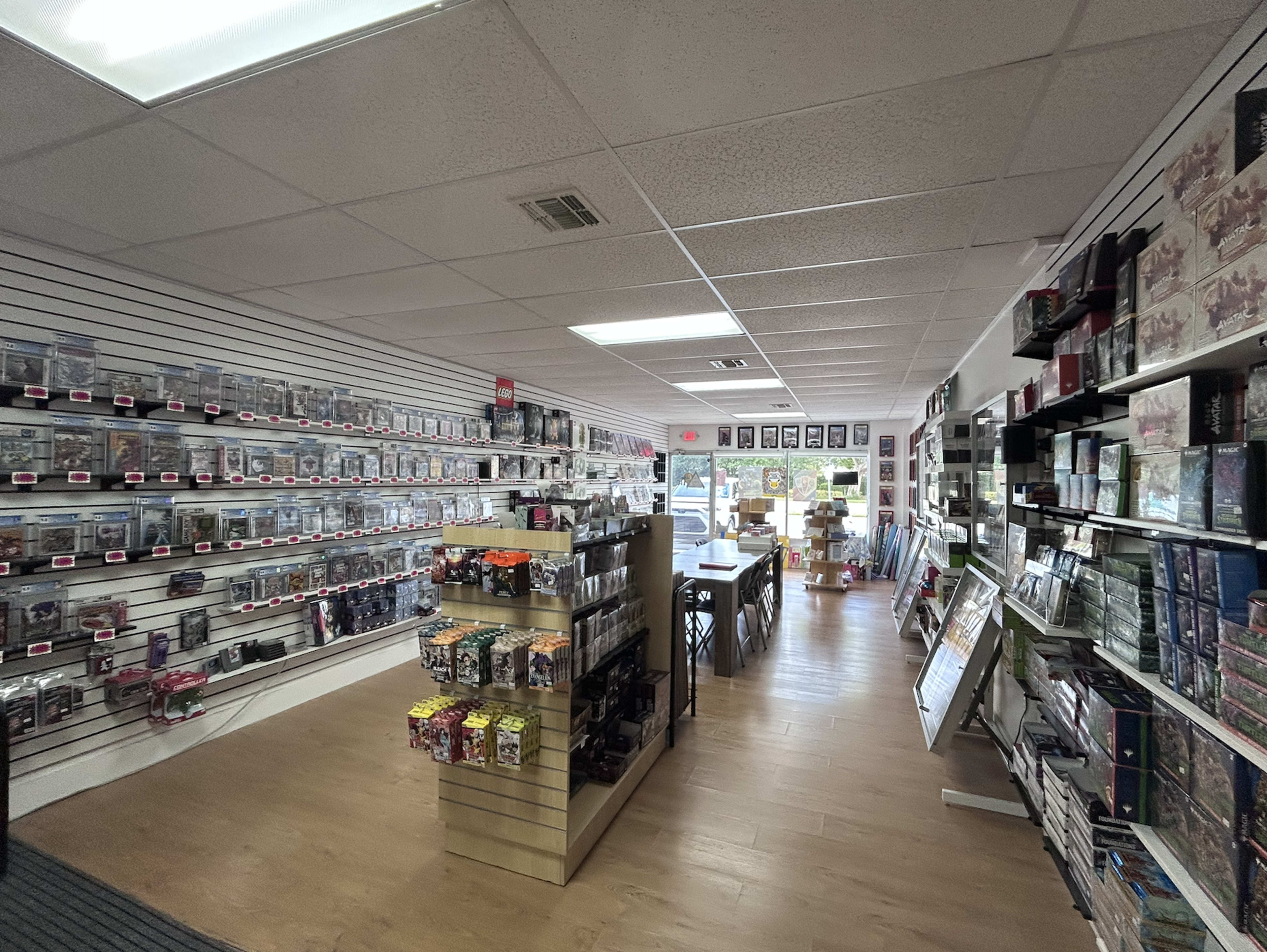 The image shows the interior of a retail store that features rows of shelves filled with merchandise, including collectibles and games, along with a table and chairs in the center.