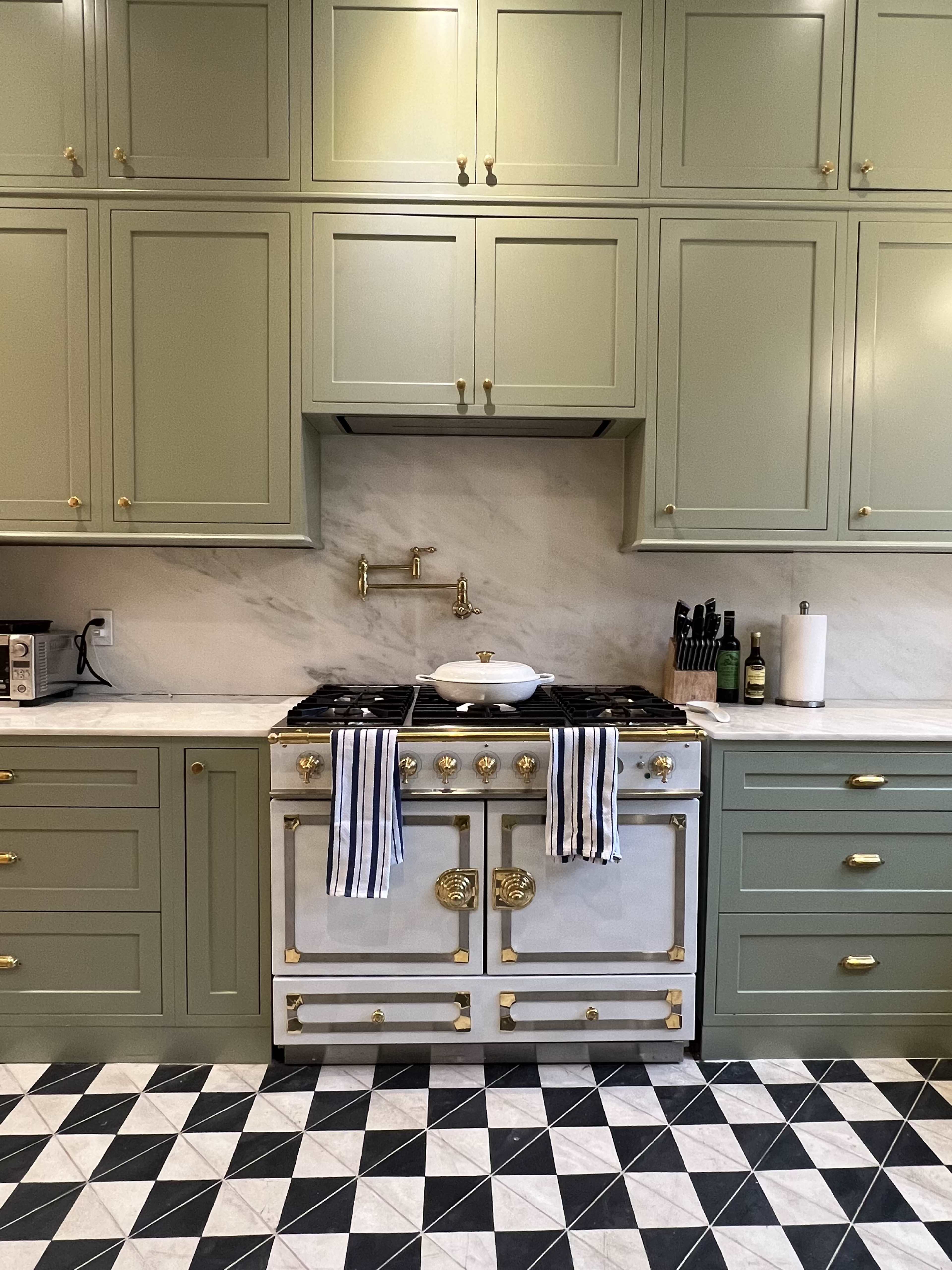 The kitchen features green cabinets, a white marble backsplash, a vintage-style stove with gold accents, and a checkerboard floor in black and white.