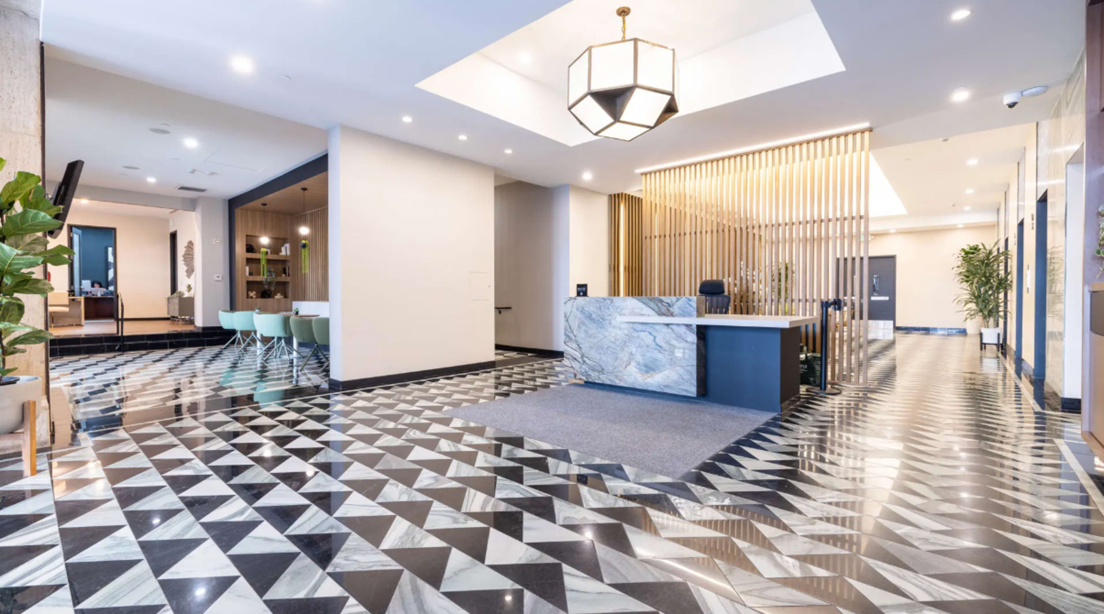 The image shows a modern lobby with a geometric black and white tiled floor, a marble reception desk, and natural light coming from a skylight.