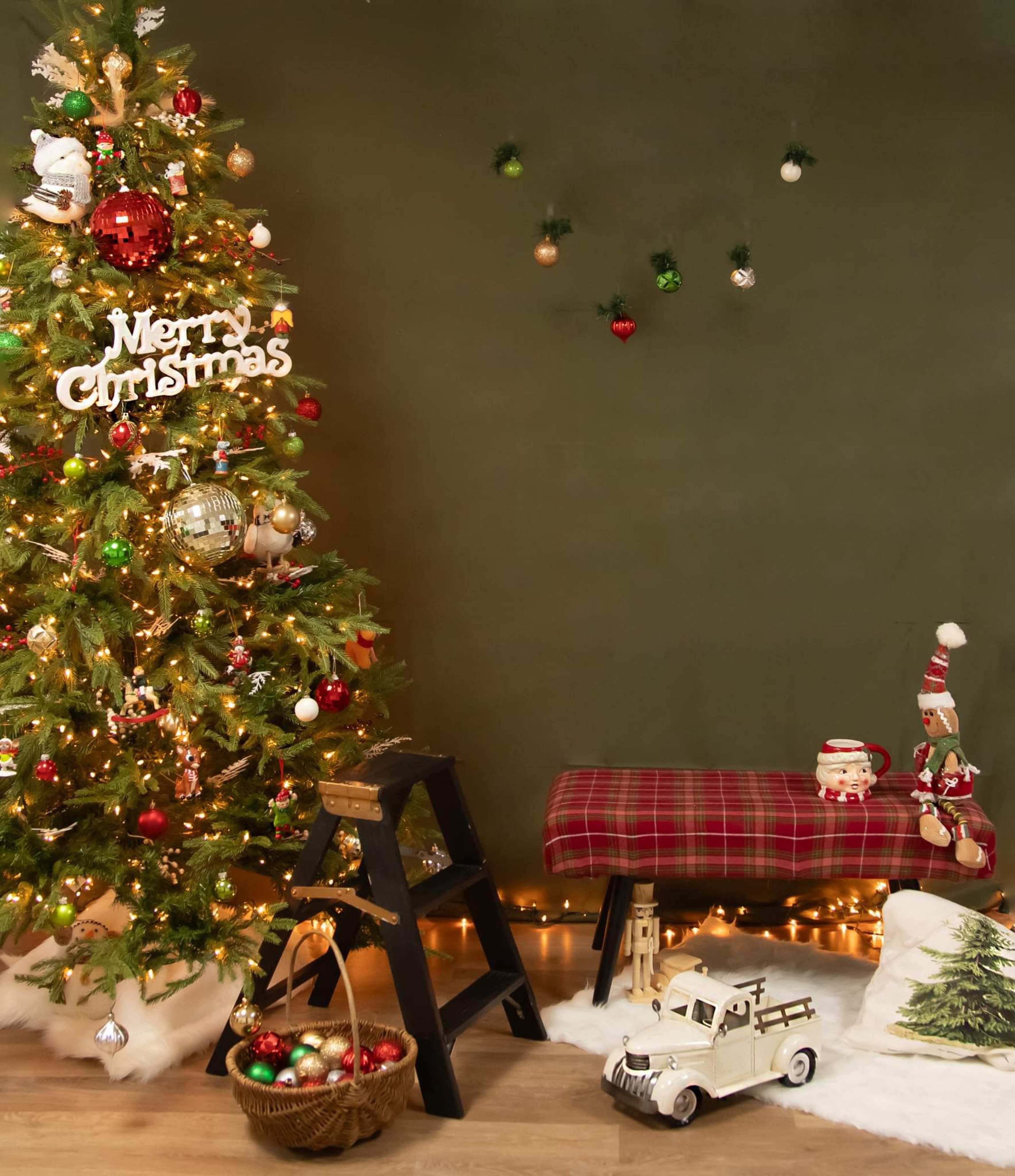 A decorated Christmas tree stands next to a bench adorned with festive items and a vintage toy truck on a snowy white base.