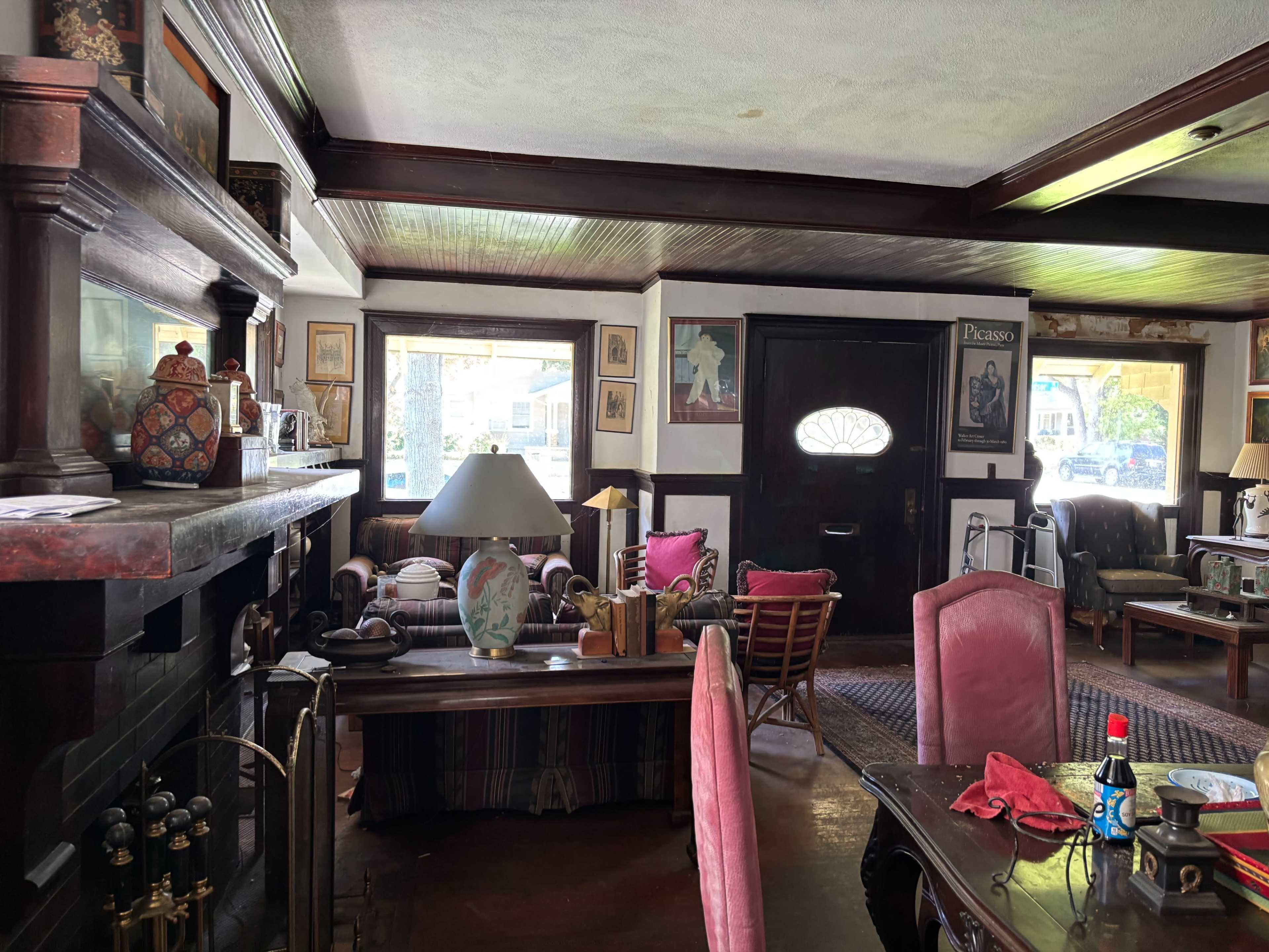 The image depicts a cozy living room with a fireplace, wooden furnishings, and various decorative artwork on the walls.