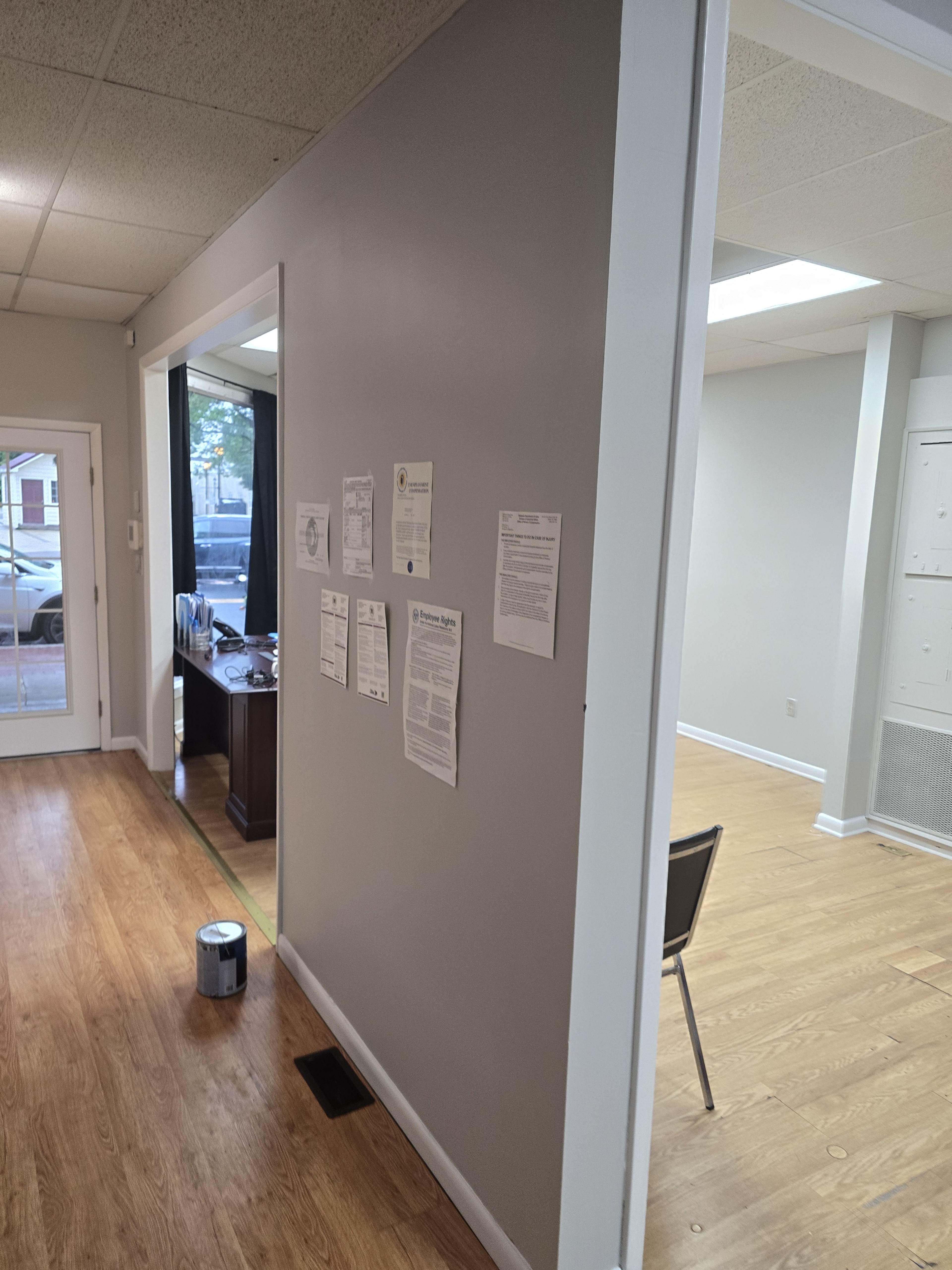 The image shows a partially finished room with a gray wall, papers mounted on it, and a chair positioned in a light-colored space beside a window.